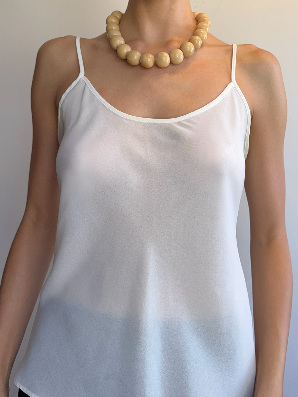 White satin camisole with a gradient hemline worn by a person against a neutral background.