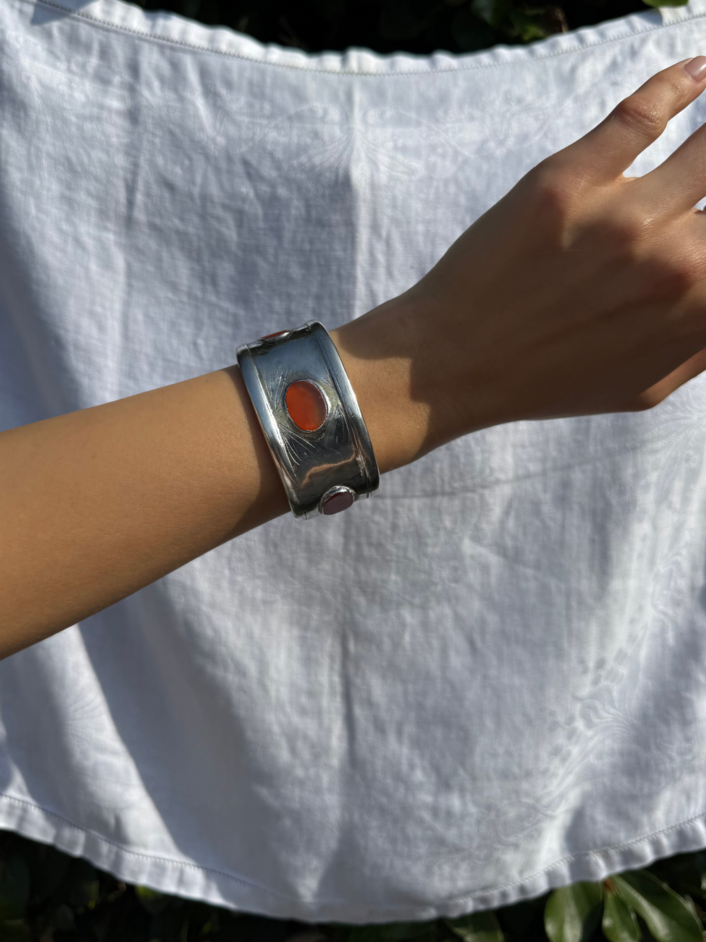 Close-up of a wrist wearing a silver bracelet with a red stone, against a white fabric background.