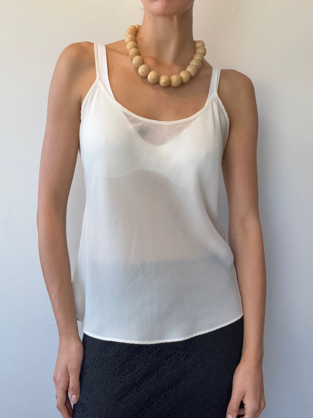 Woman wearing a white tank top and black skirt with a plain background