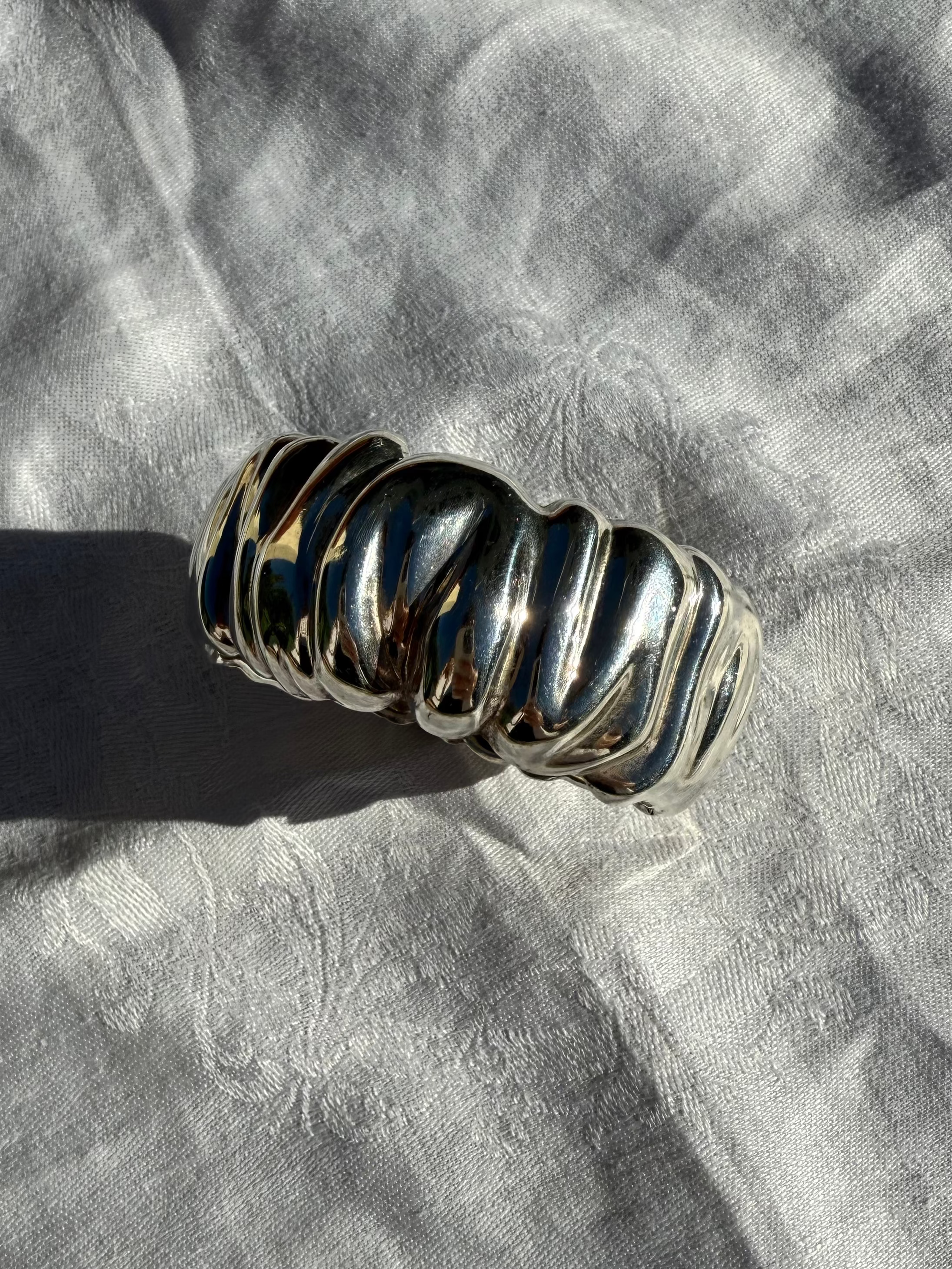 Silver ring with ribbed design on a textured gray fabric background