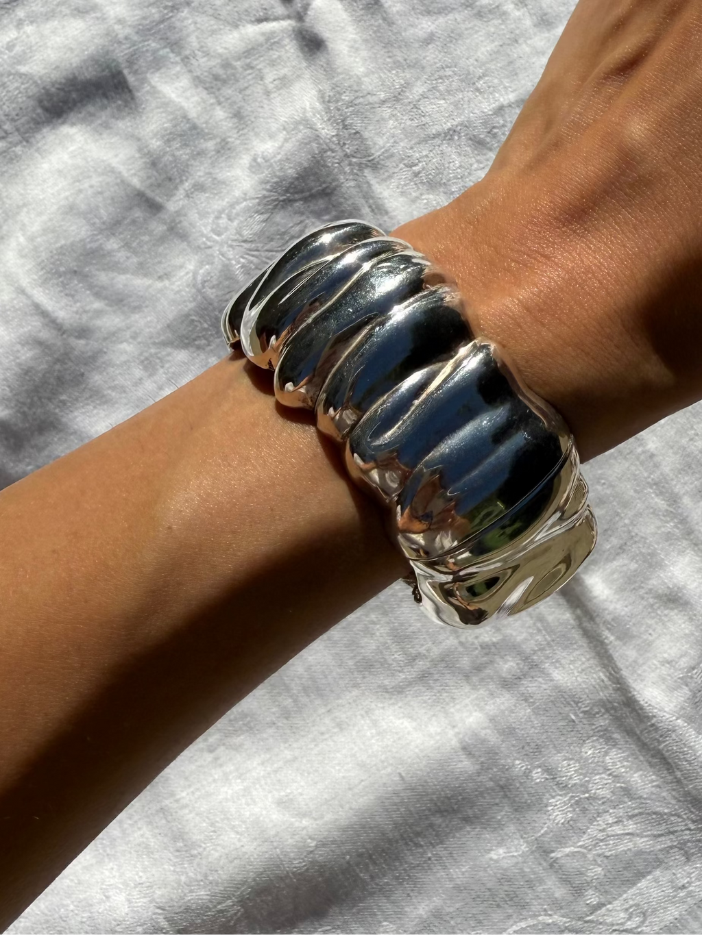 Silver bracelet on a wrist against a light gray background