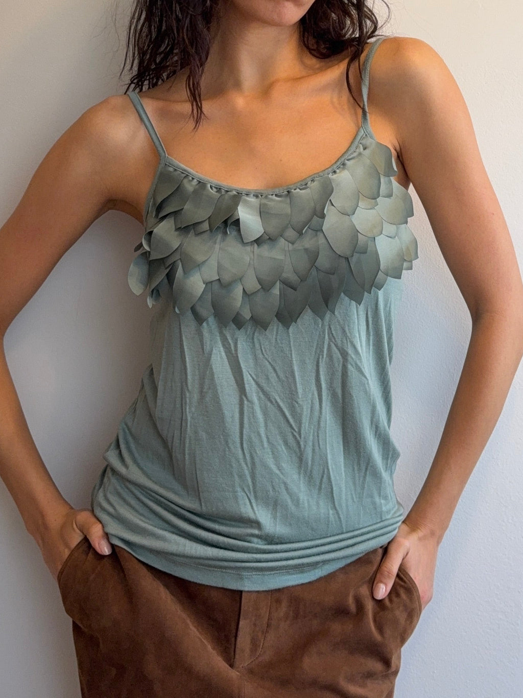 Woman lying on a plain surface wearing a light blue dress with floral details and brown pants.