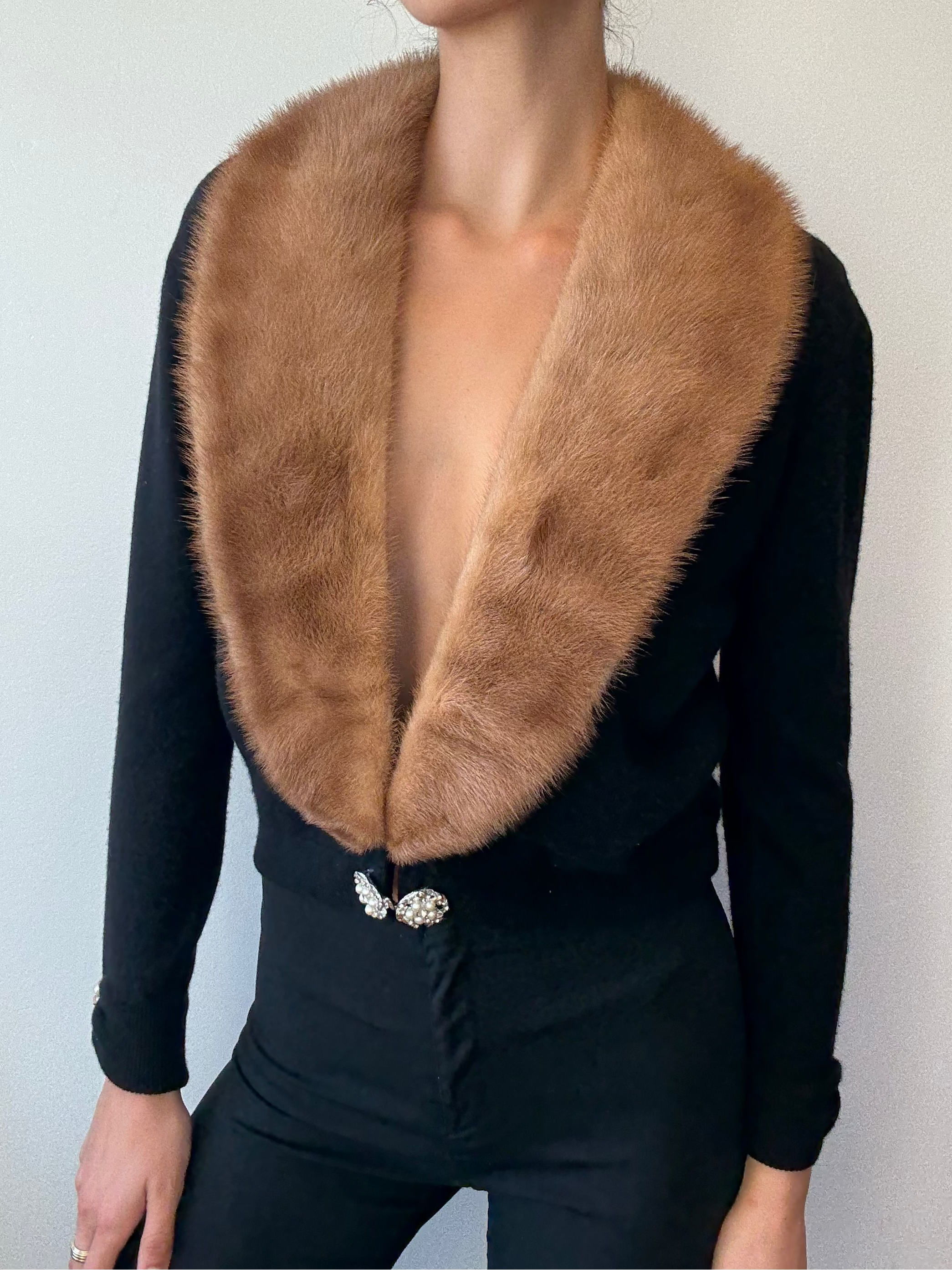 Woman wearing a black outfit with a brown fur collar against a plain background