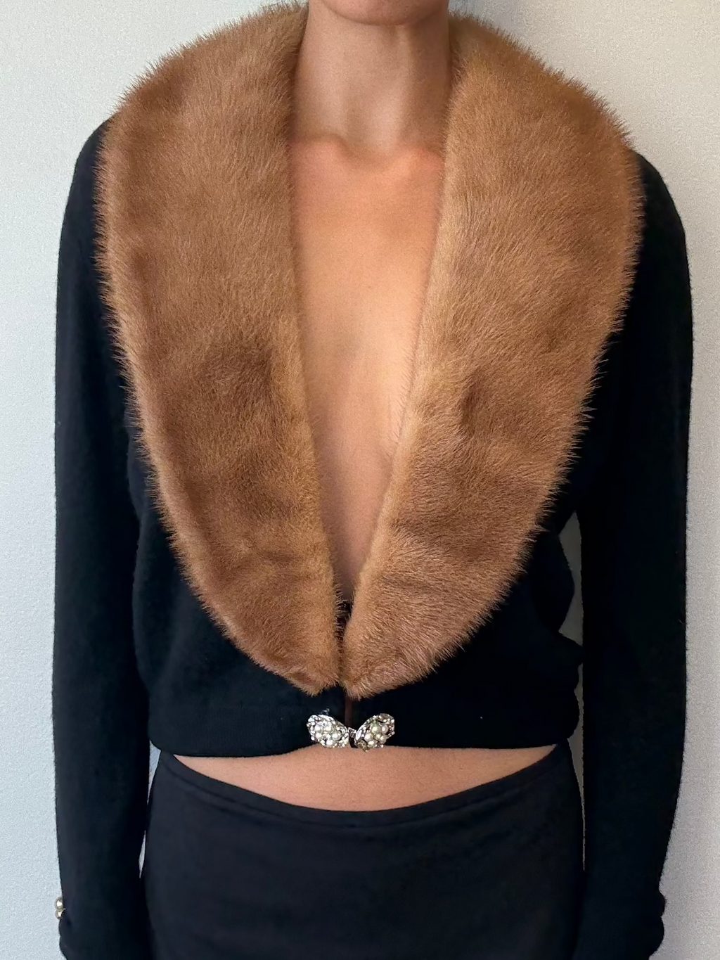 Person wearing a black top with a brown fur collar against a plain background