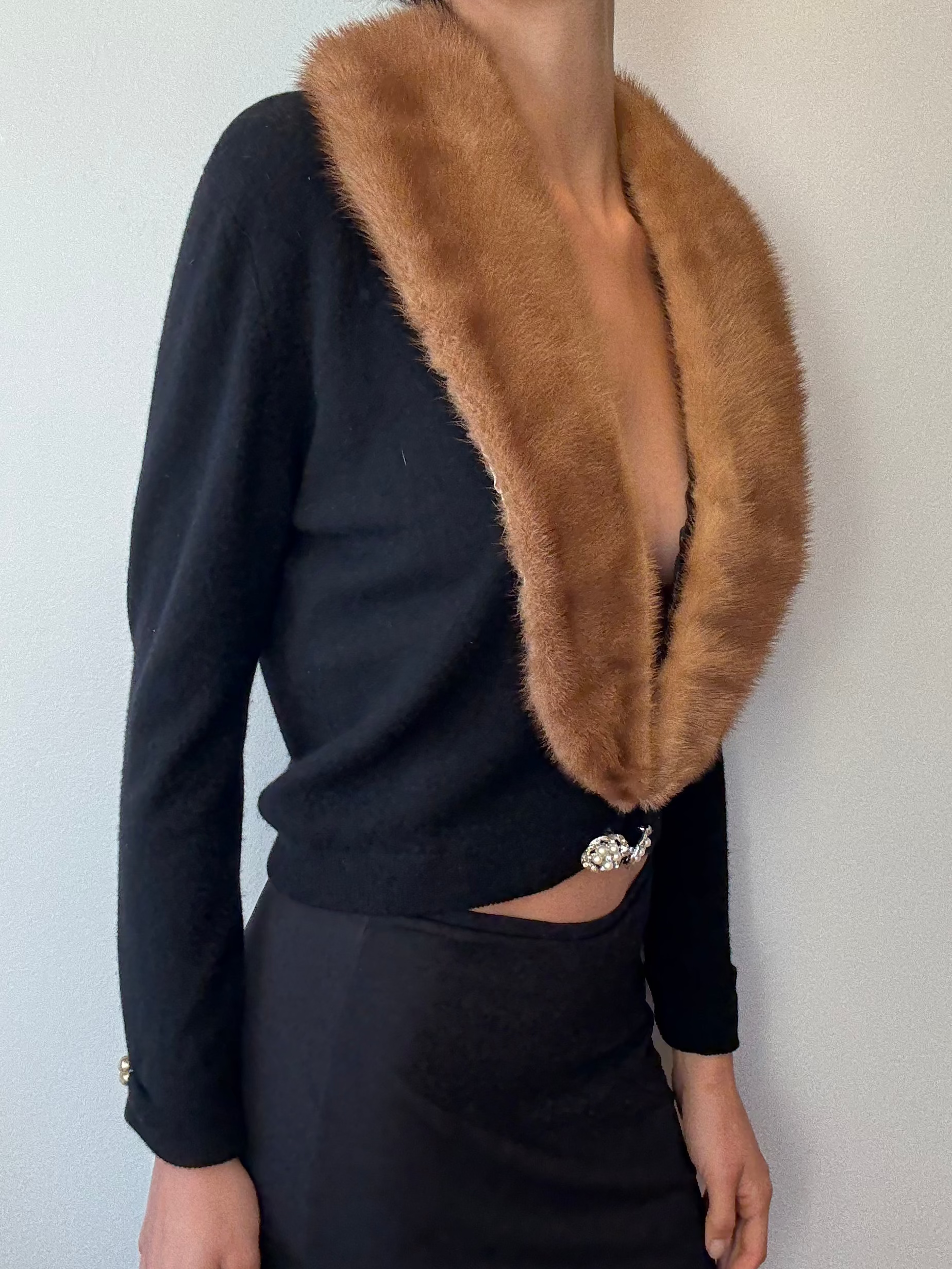 Person wearing a black outfit with a brown fur collar against a plain background