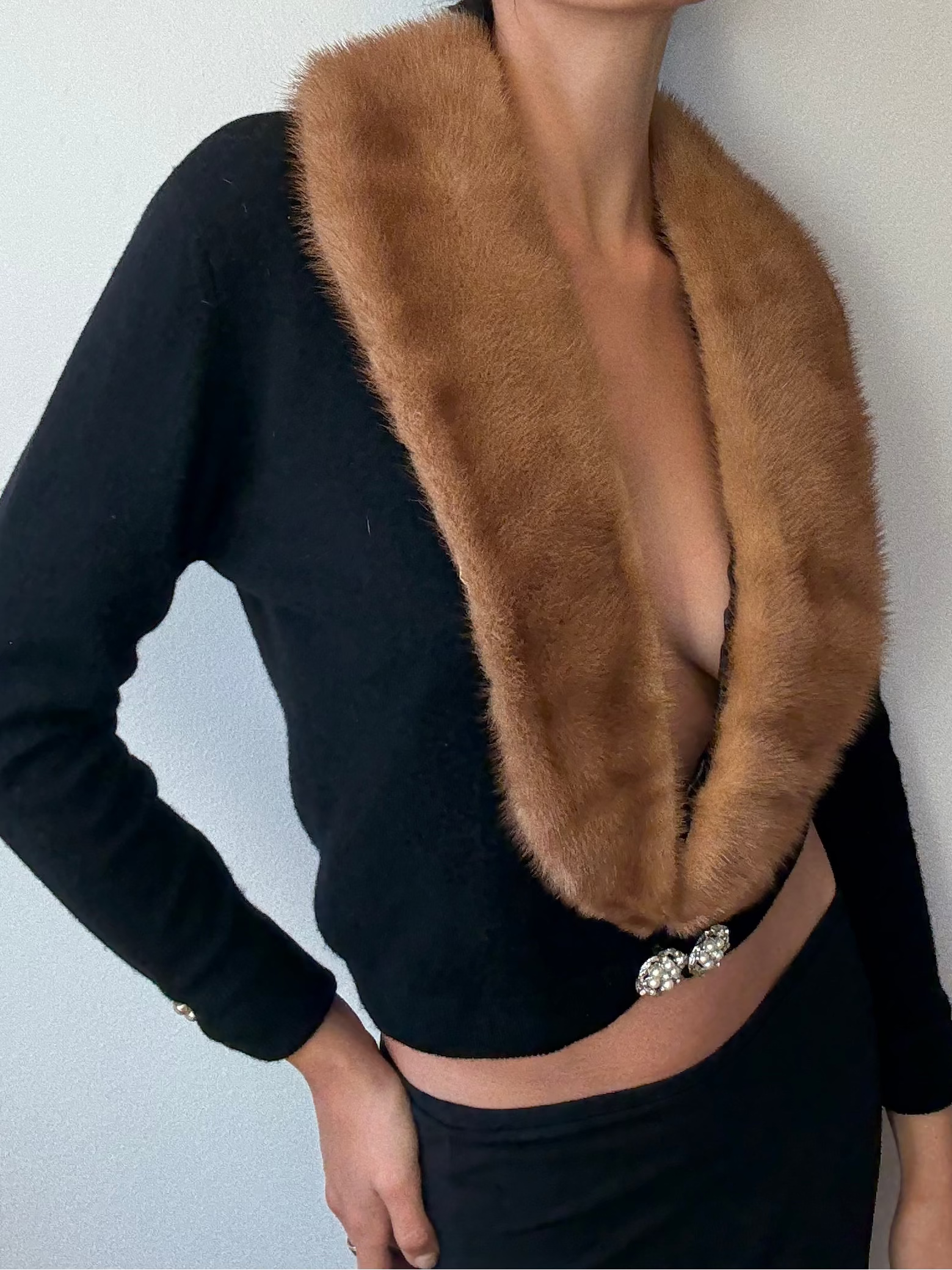 Woman wearing a black top with a brown fur collar against a plain background