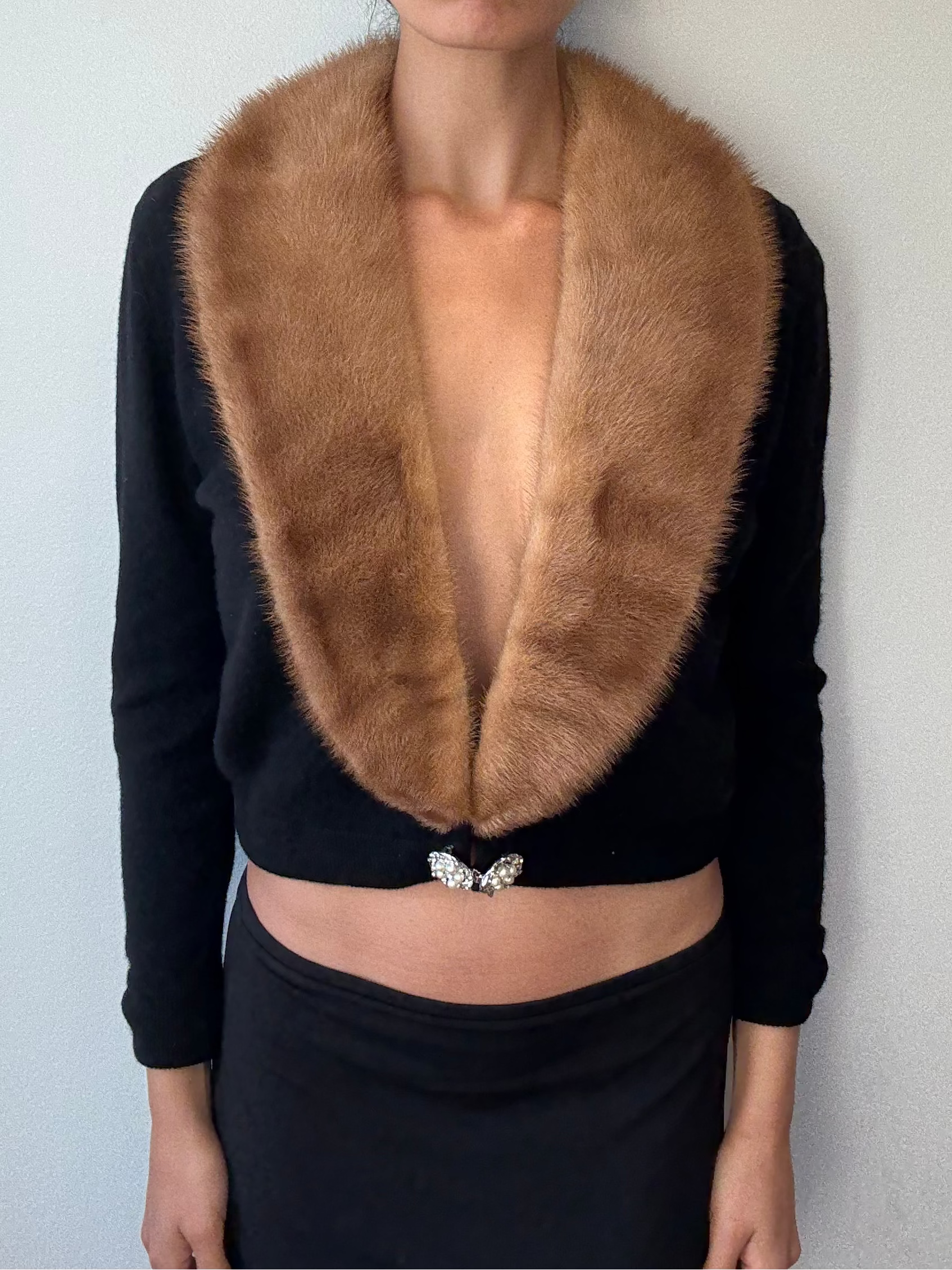 Woman wearing a black top with a fur collar against a plain background