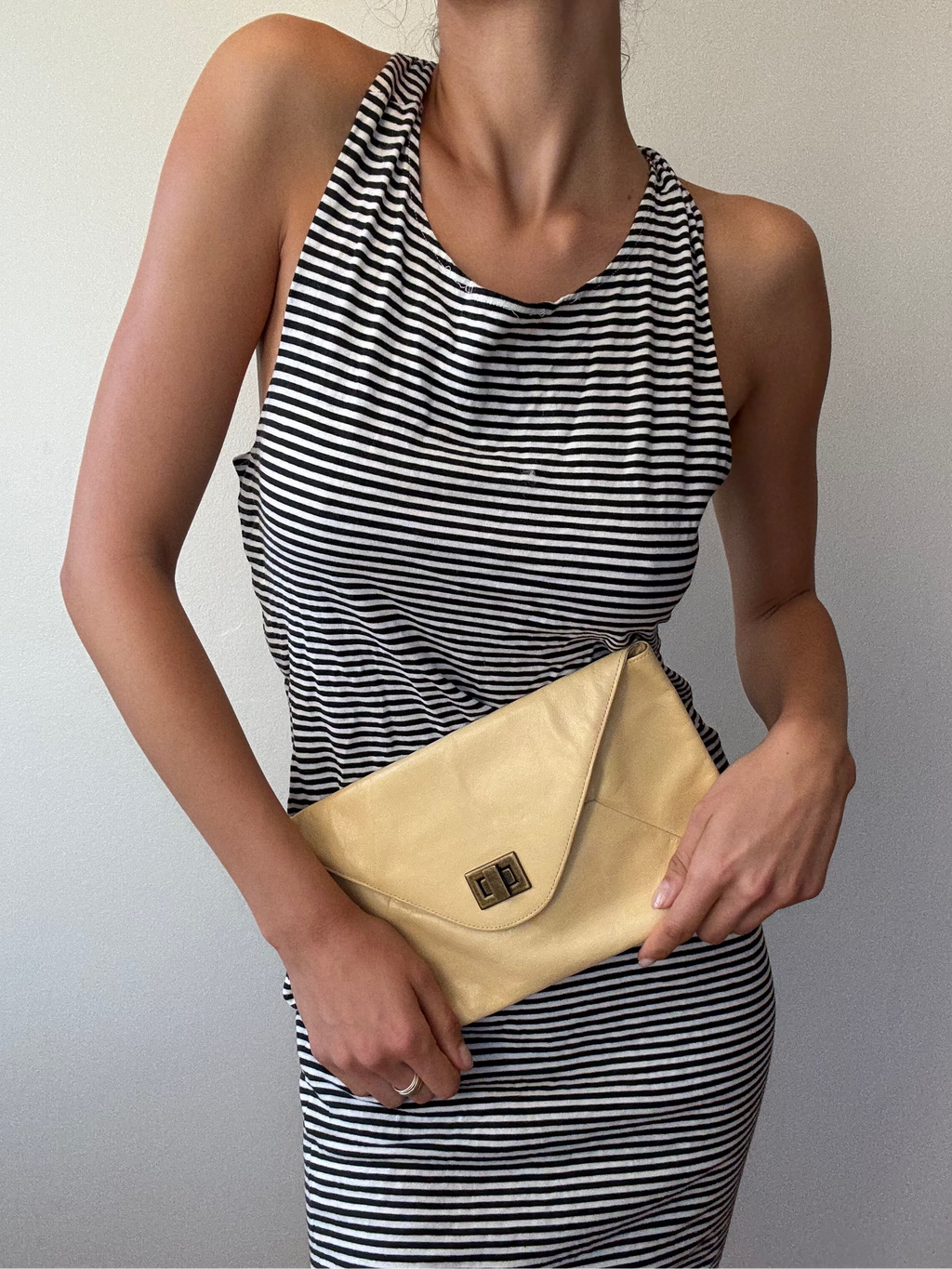 Woman holding a beige clutch bag against a plain background