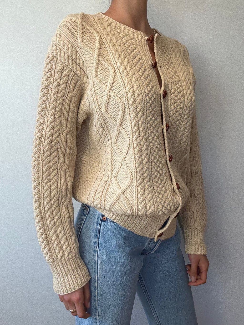 Person wearing a beige knitted cardigan with button details against a plain background