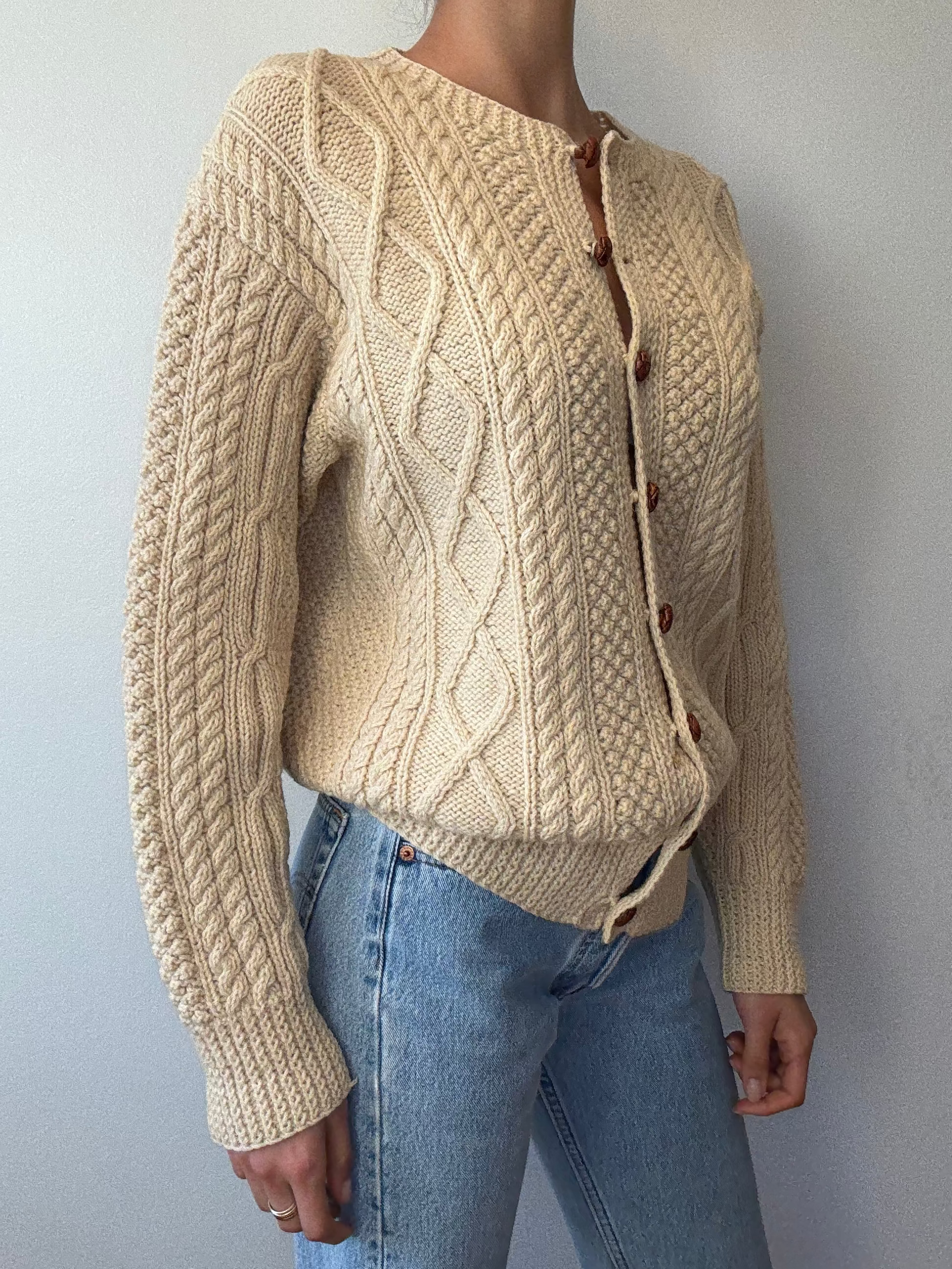 Person wearing a beige knitted cardigan with button details against a plain background