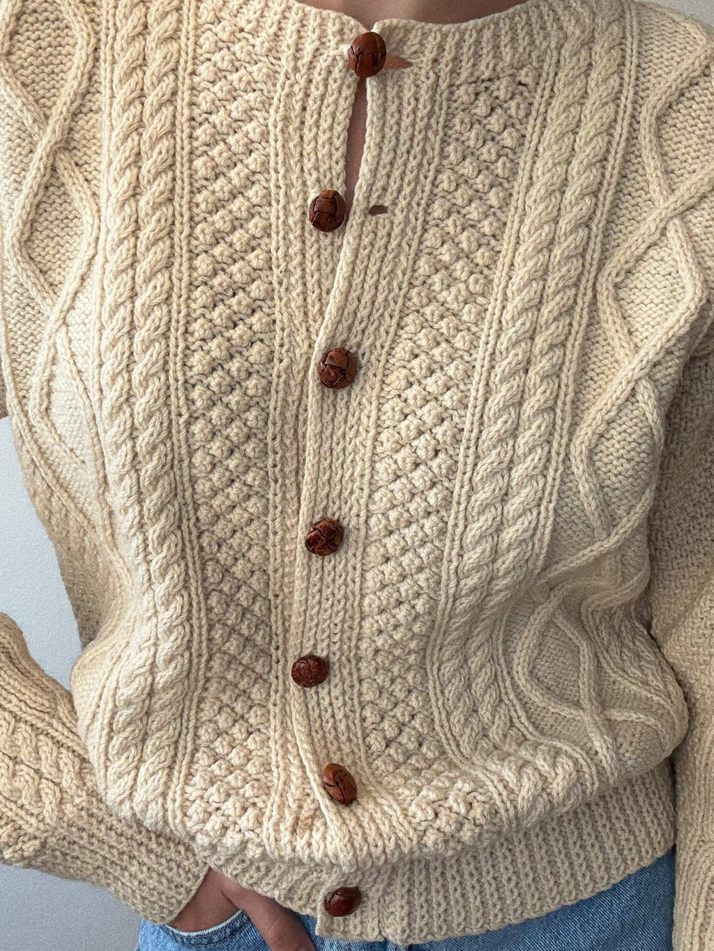 Beige knitted sweater with brown buttons on a plain background