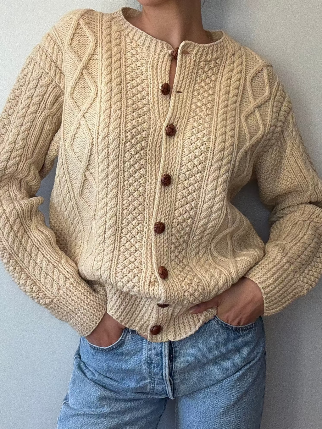 Woman wearing a beige cable knit sweater with brown buttons against a plain background
