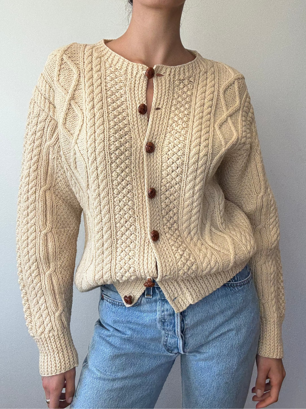 Person wearing a beige knitted cardigan with brown buttons against a plain background