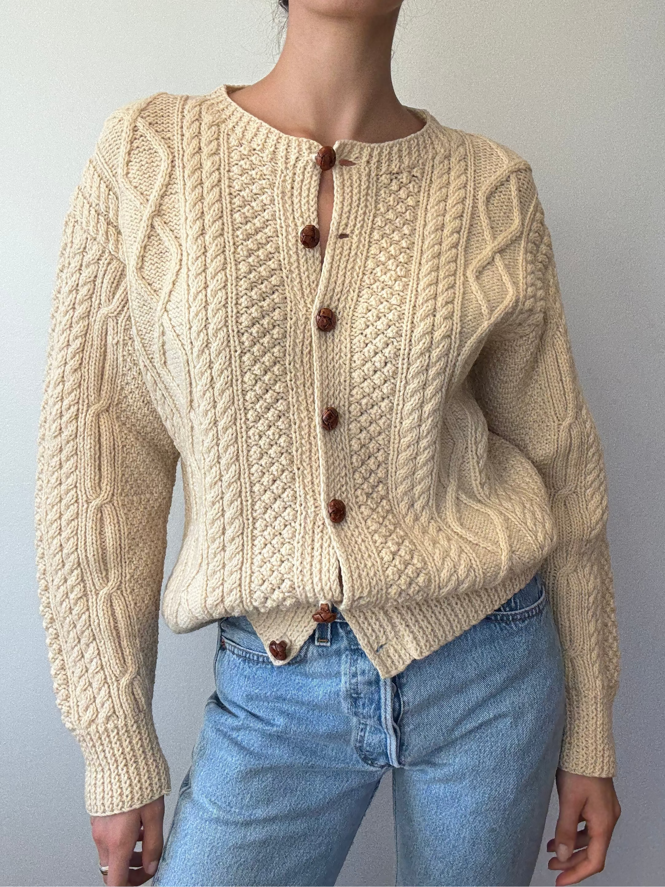 Person wearing a beige knitted cardigan with brown buttons against a plain background
