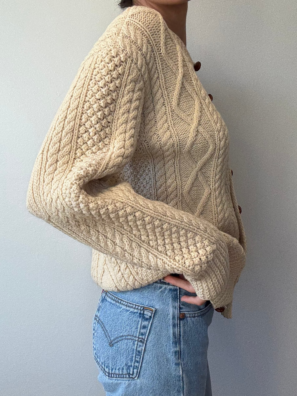 Person wearing a beige knitted sweater and blue jeans against a plain background