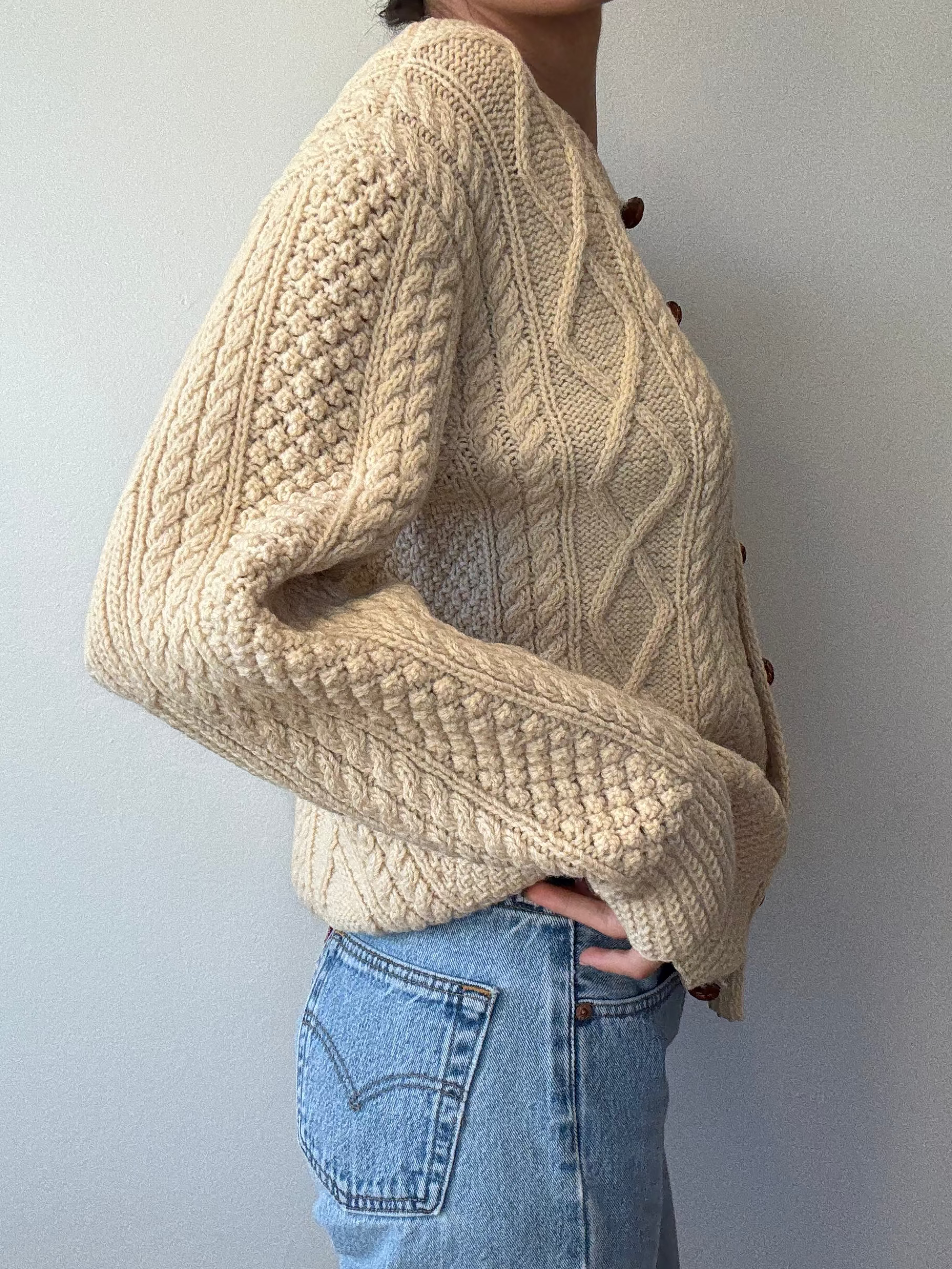 Person wearing a beige knitted sweater and blue jeans against a plain background