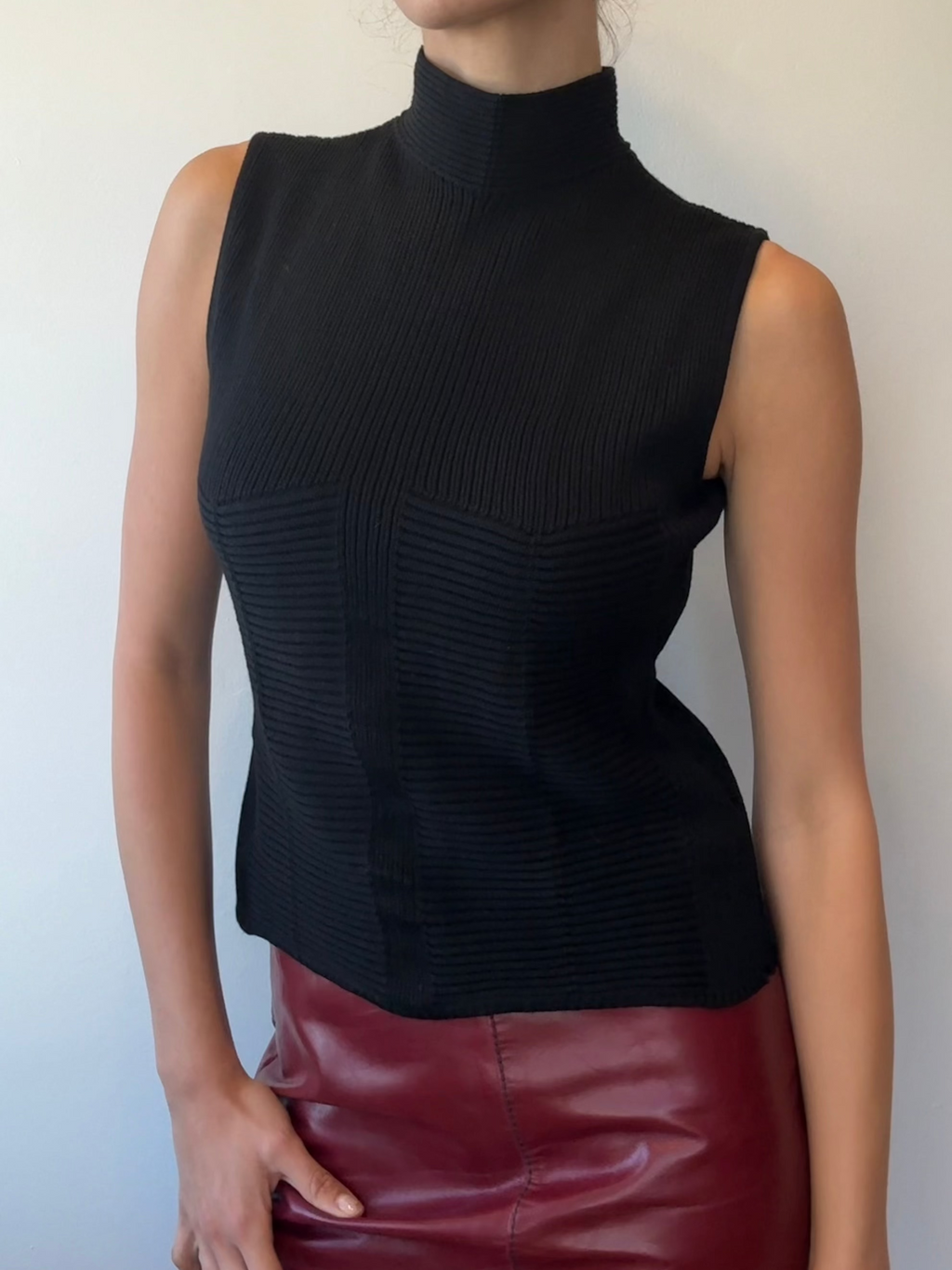 Woman wearing a black sleeveless top and red leather skirt against a plain background