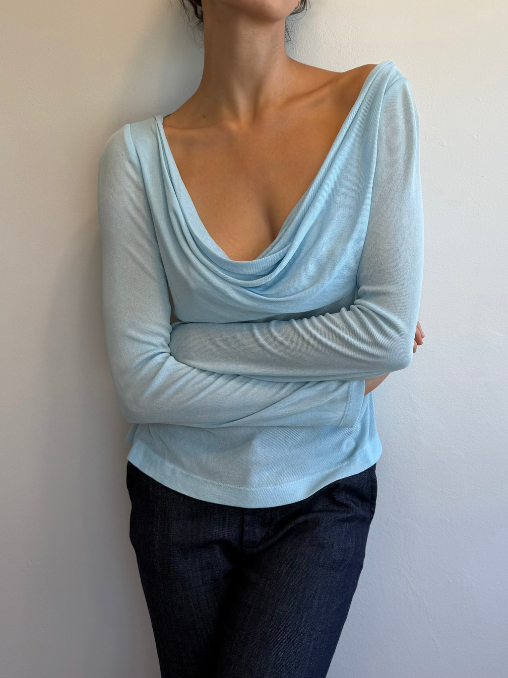 Person wearing a light blue long-sleeve top and dark pants against a plain background