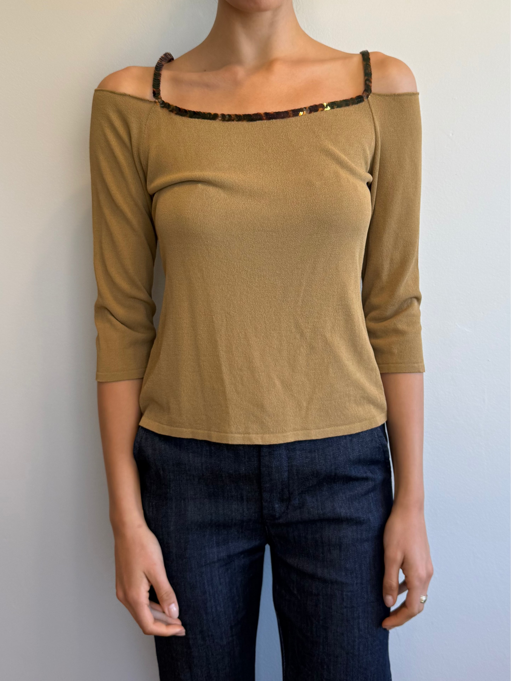 Woman wearing a beige off-shoulder top and dark jeans against a plain background