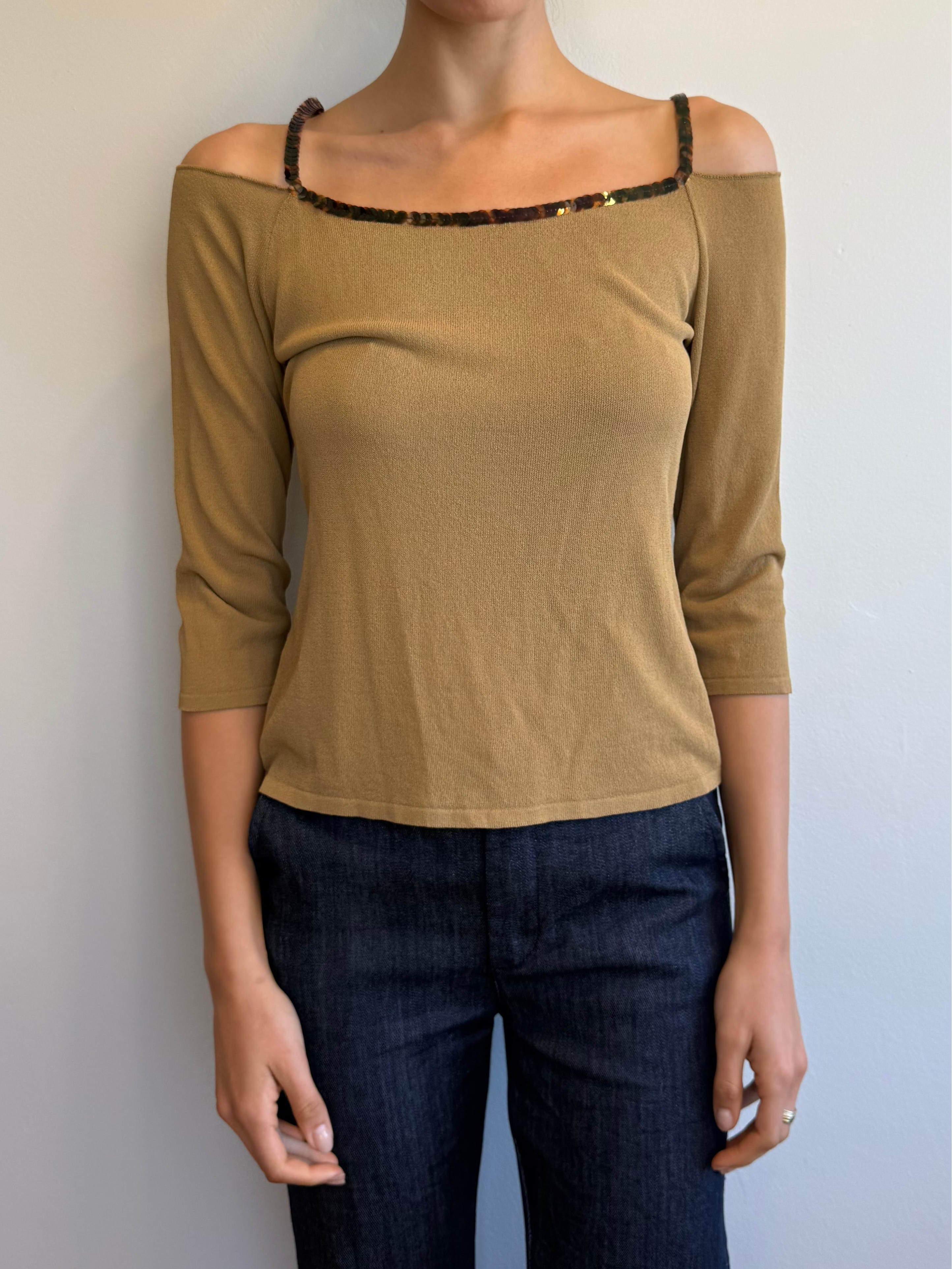 Woman wearing a beige off-shoulder top and dark jeans against a plain background