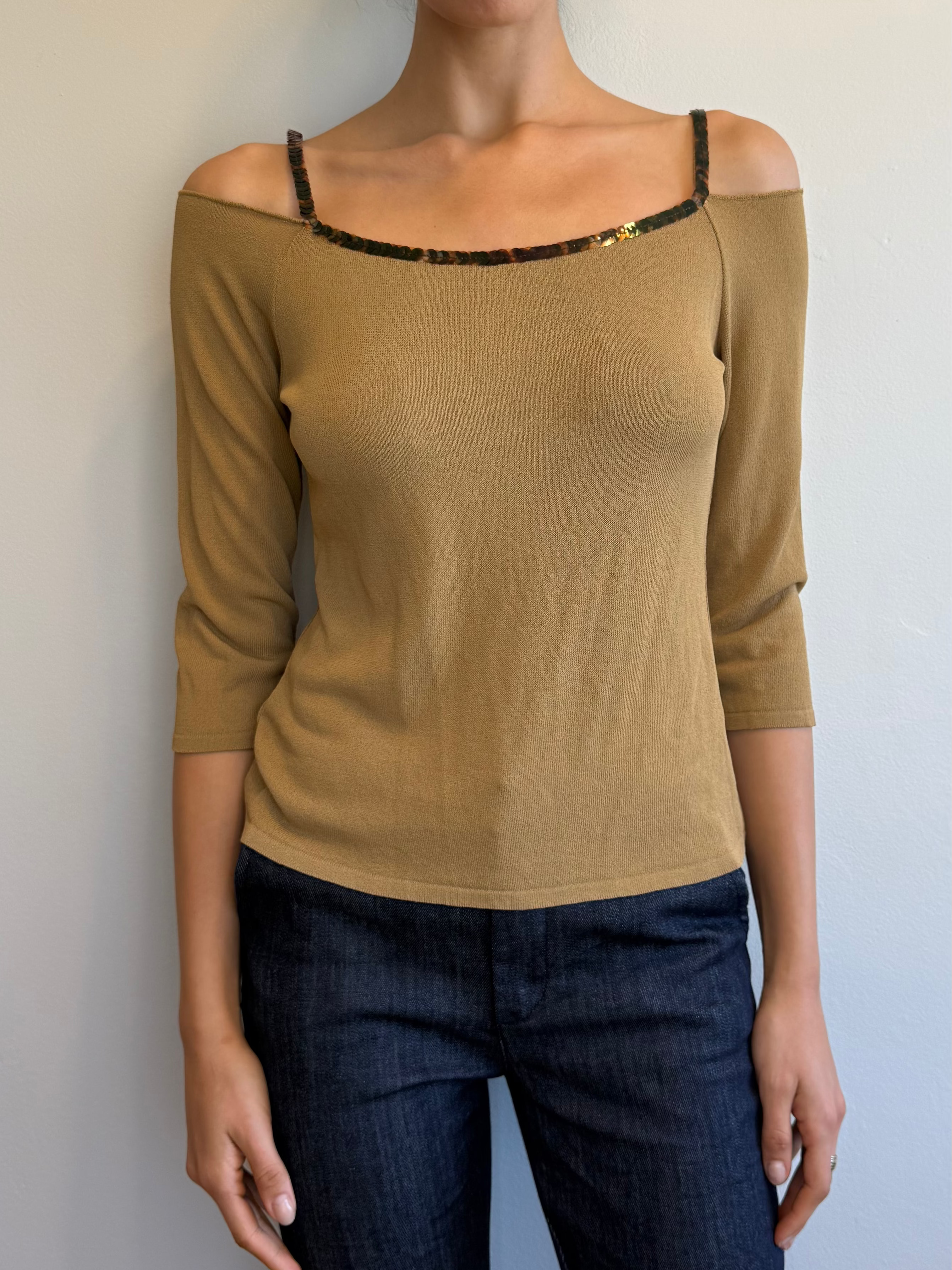 Woman wearing a beige top and dark jeans against a plain background