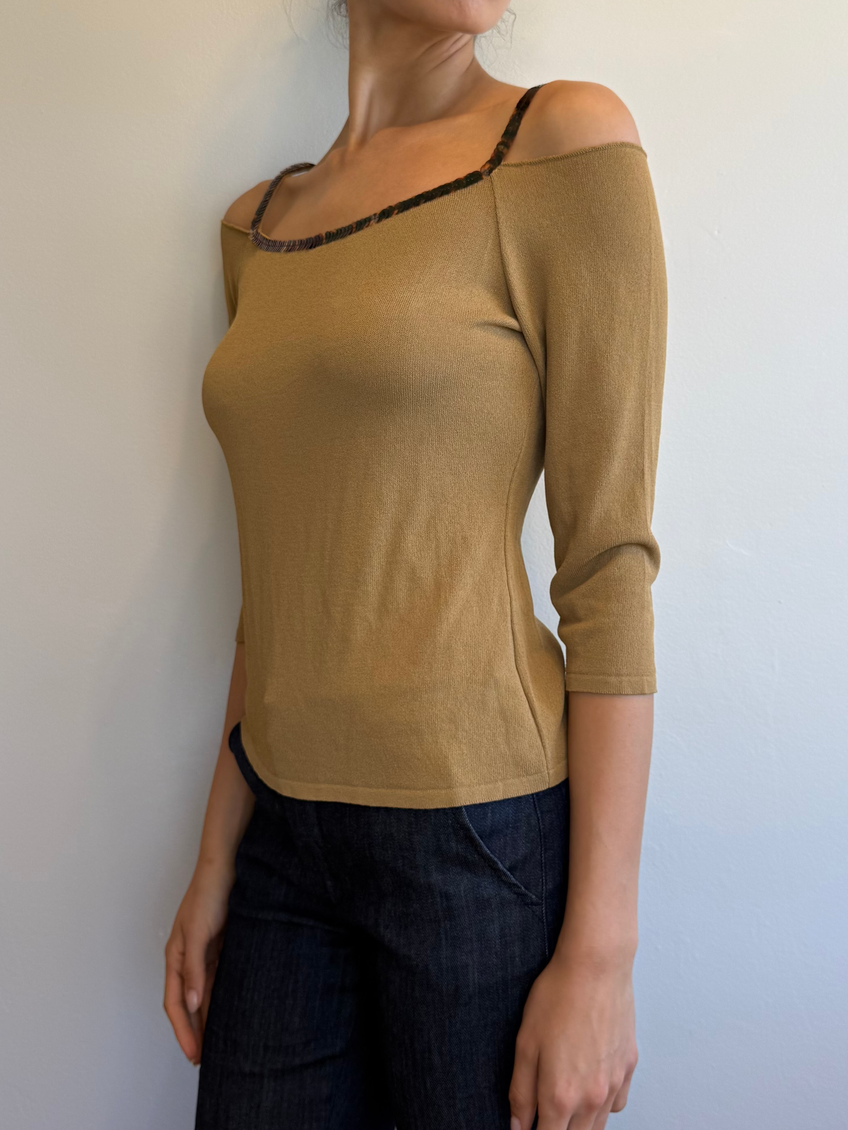 Woman wearing a beige top and dark pants against a plain background