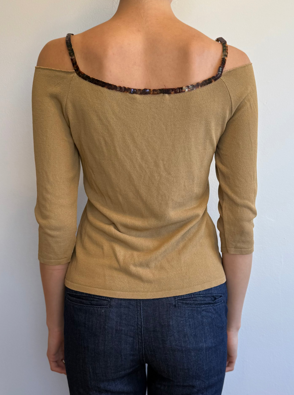 Person wearing a beige top with a leopard print trim and dark blue jeans against a plain background