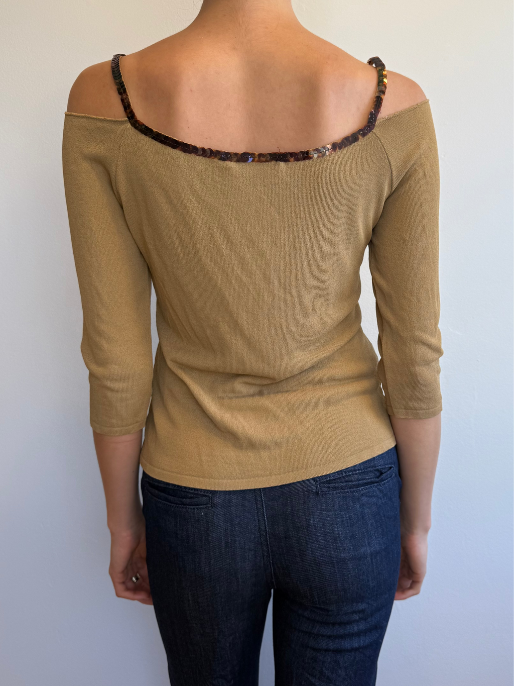 Person wearing a beige off-shoulder top and dark jeans against a white background