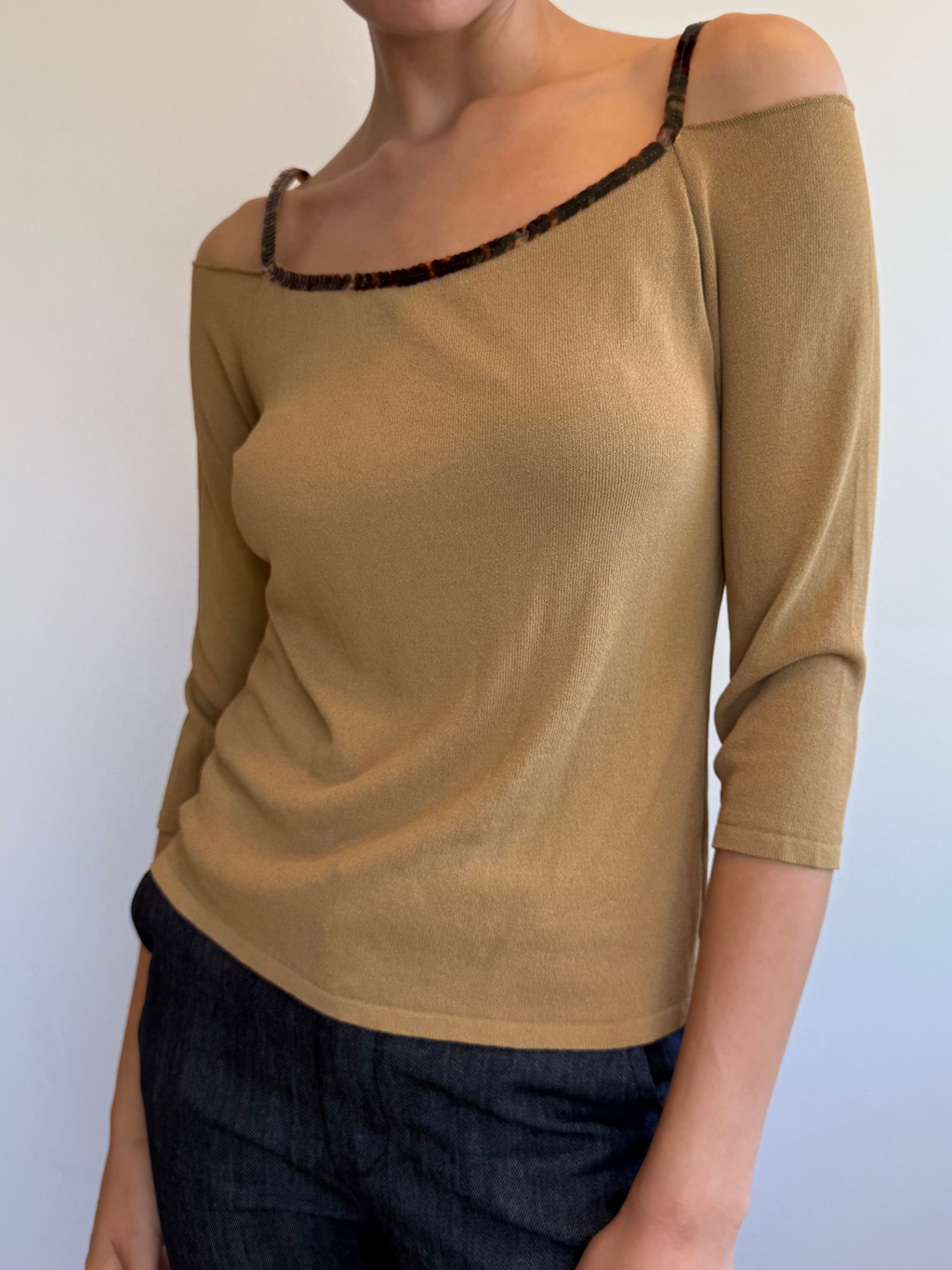 Woman wearing a beige top with black lace trim against a plain background