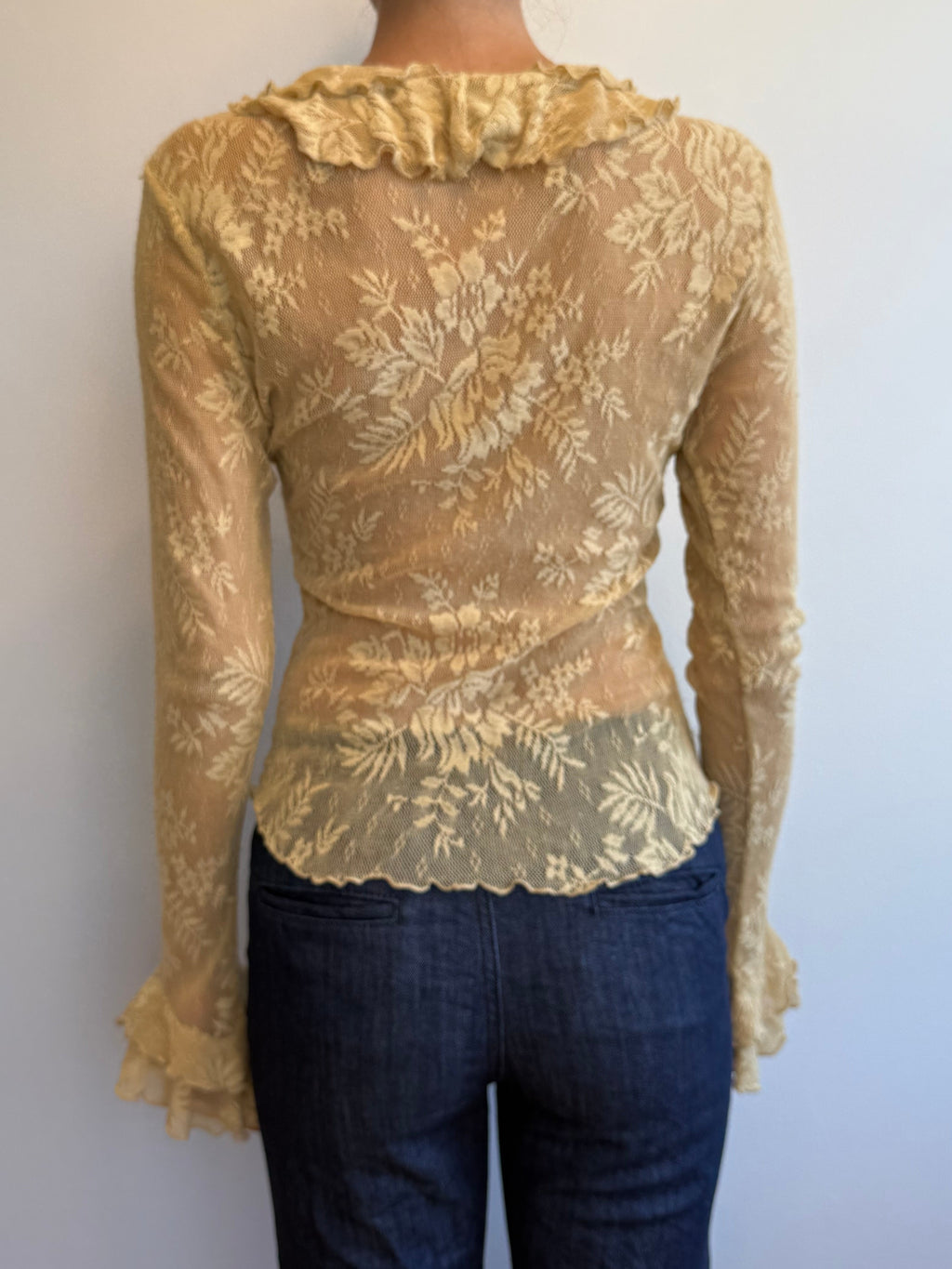 Person wearing a beige lace top and dark jeans on a plain background