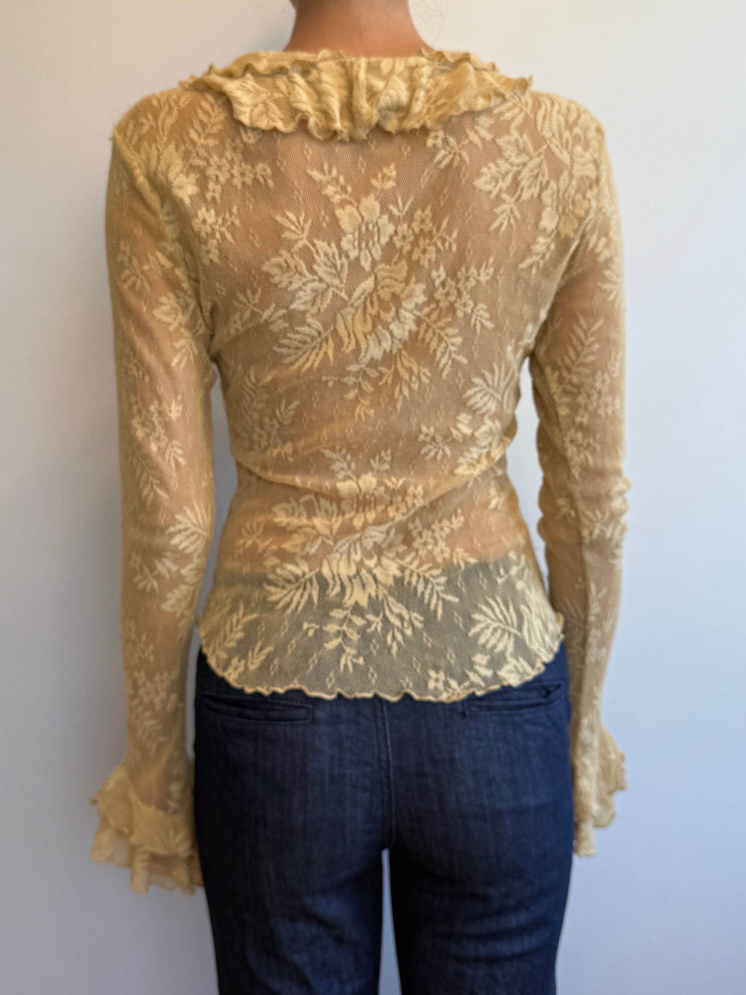 Person wearing a beige lace top and dark jeans on a plain background