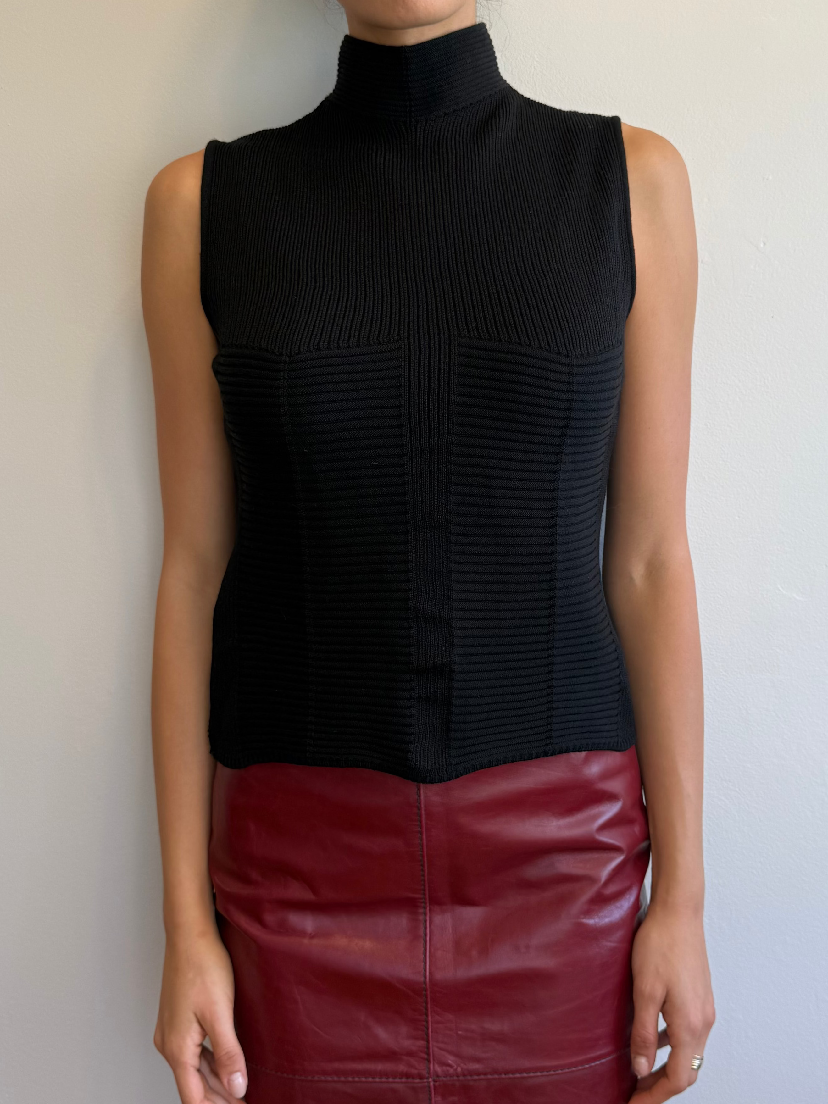 Woman wearing a black sleeveless top and red leather skirt against a plain background