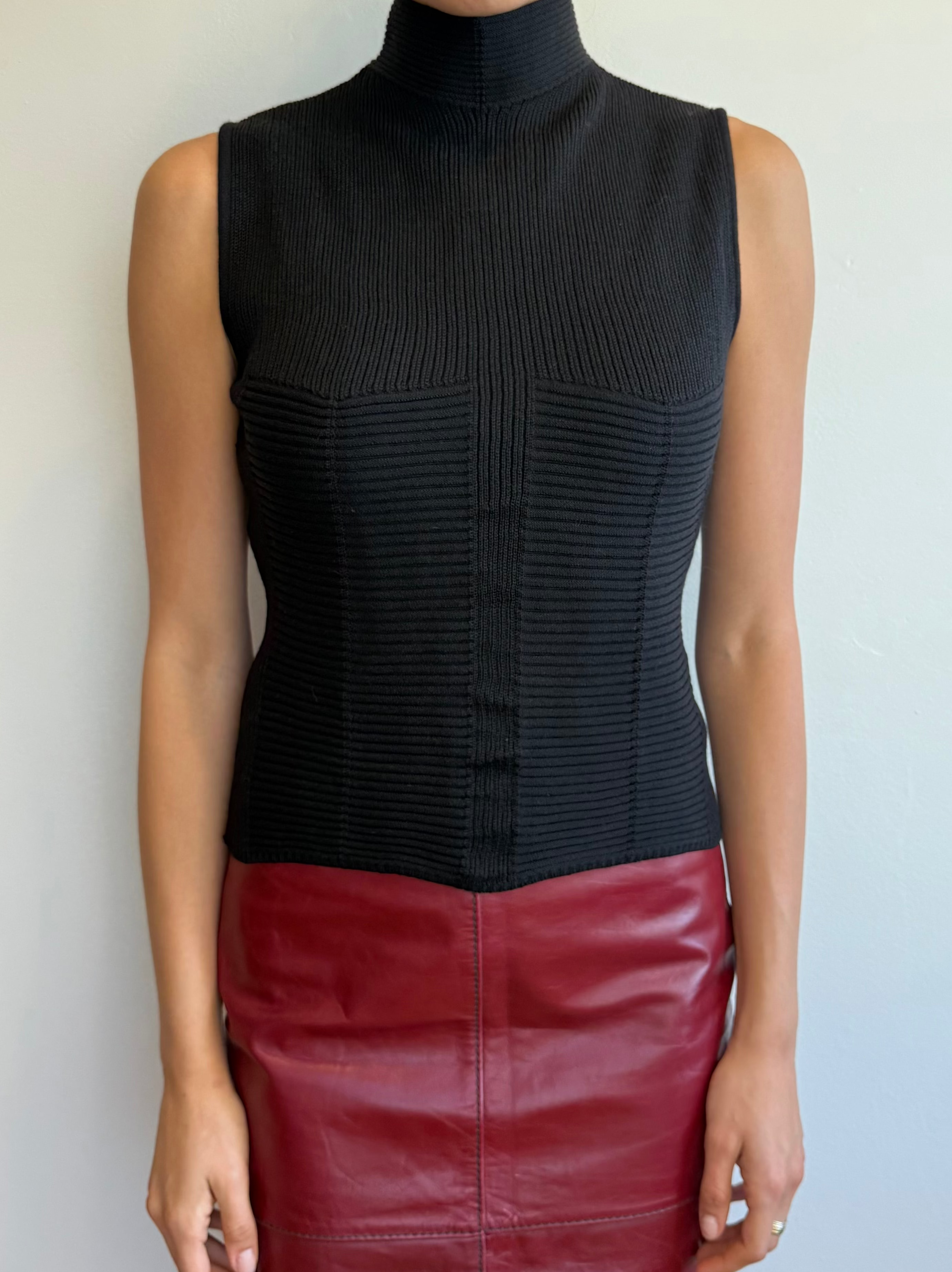 Person wearing a black sleeveless top and red leather skirt against a plain background