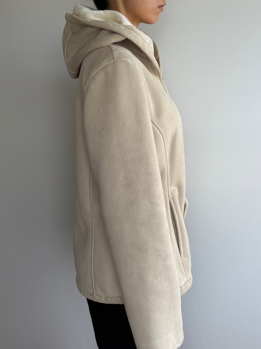 Person wearing a beige hoodie against a plain wall