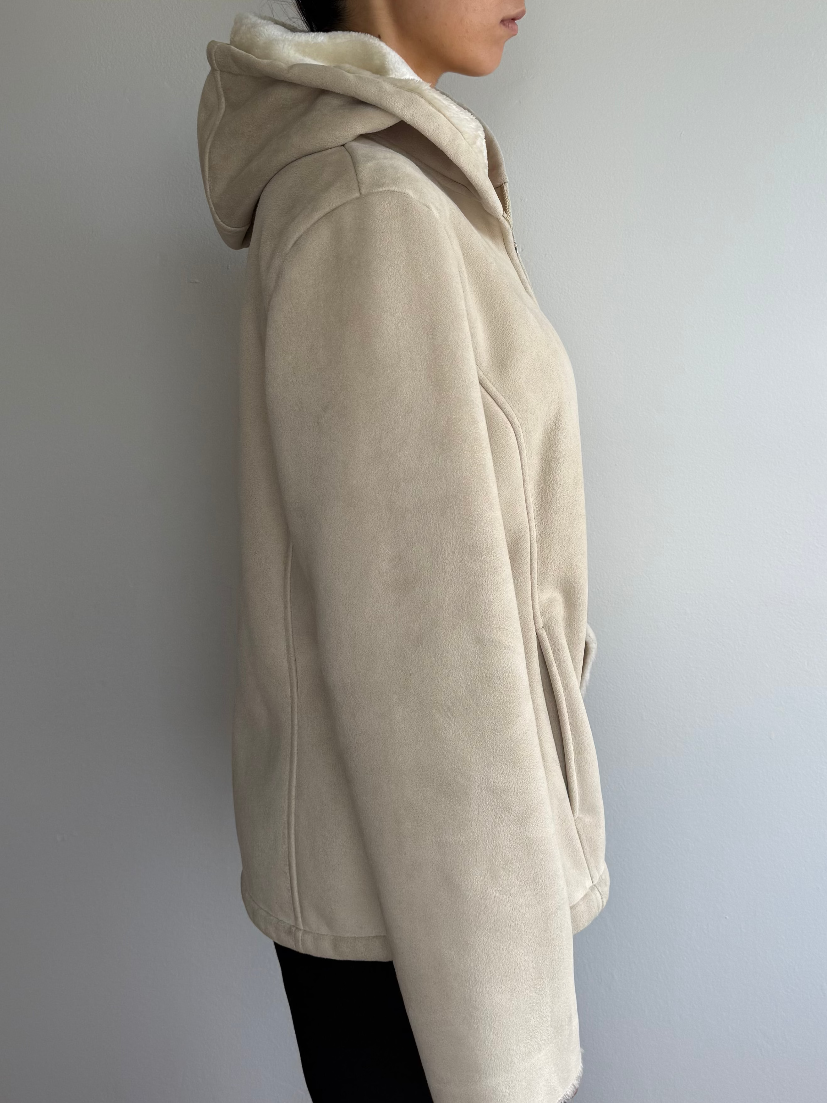Person wearing a beige hoodie against a plain wall