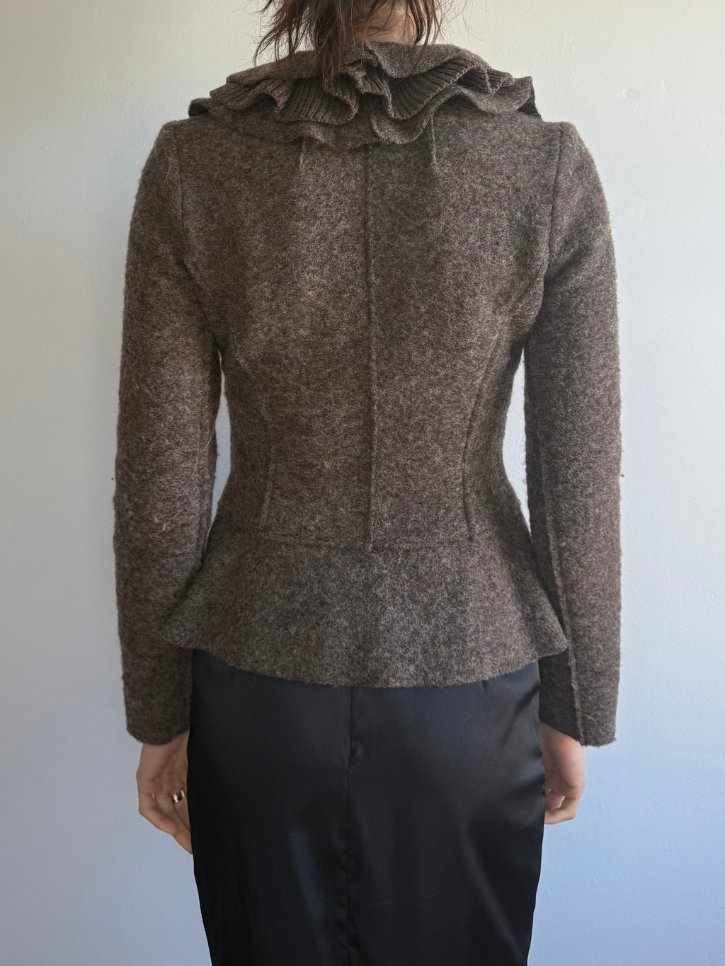 Person wearing a brown jacket with ruffled details on a plain background