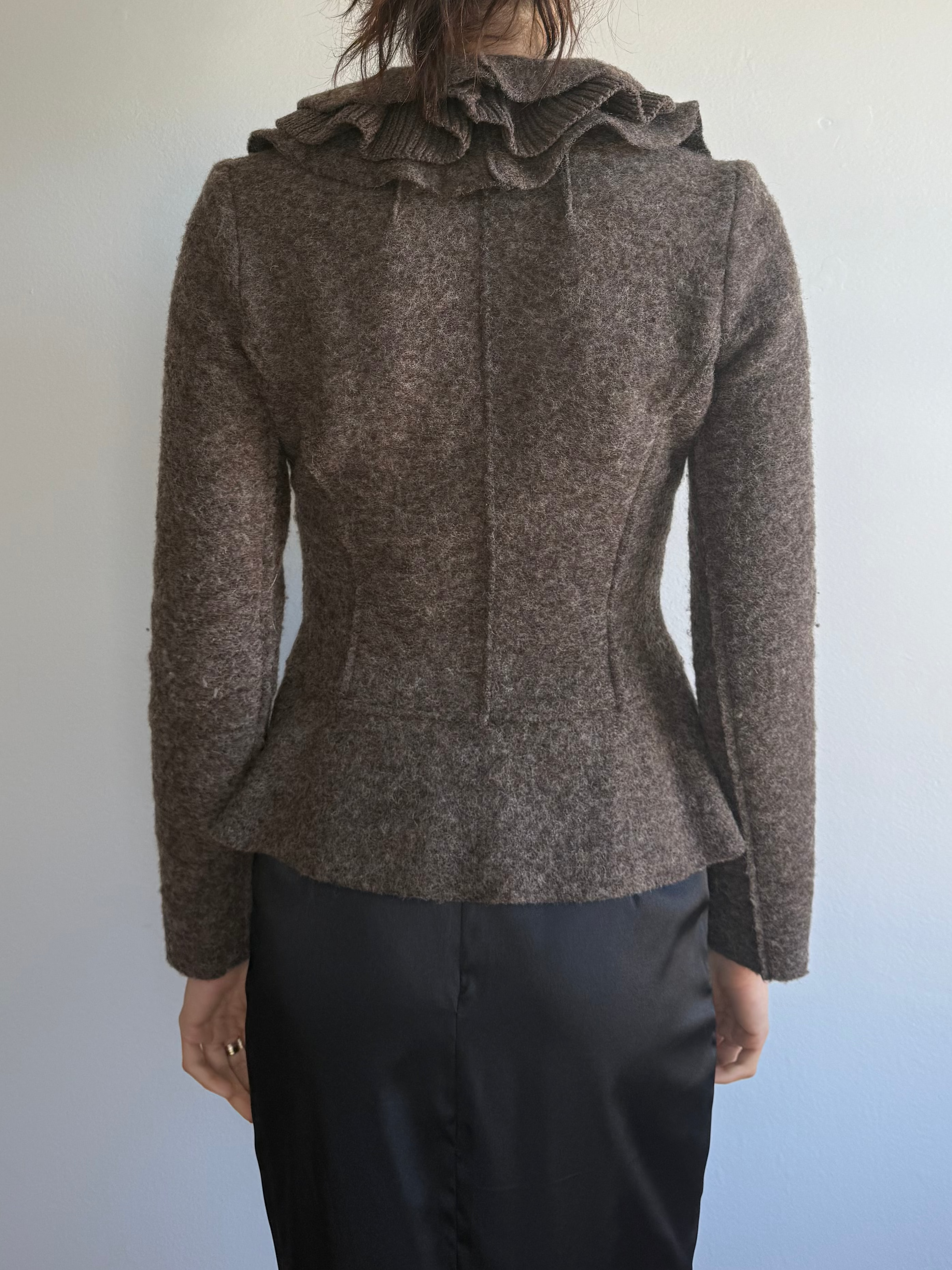 Person wearing a brown jacket with ruffled details on a plain background