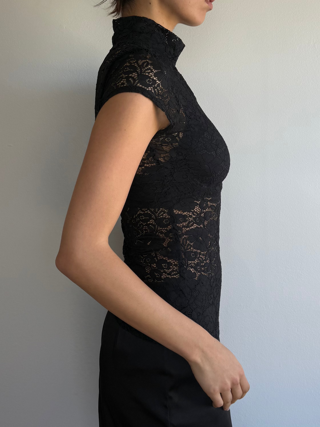 Woman wearing a black lace dress against a plain wall