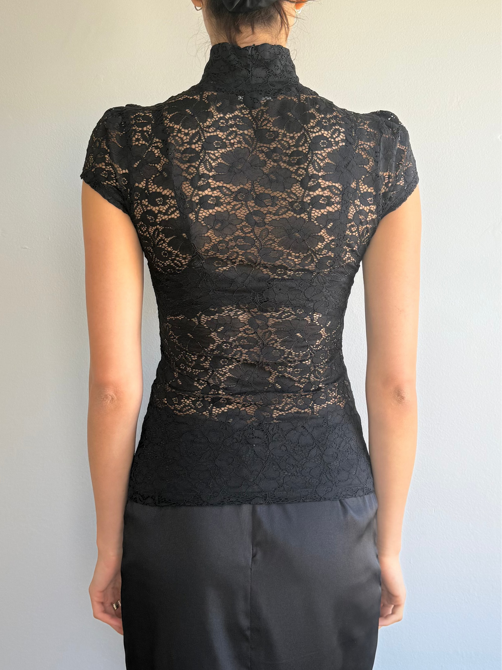Person wearing a black lace top and black pants against a plain background
