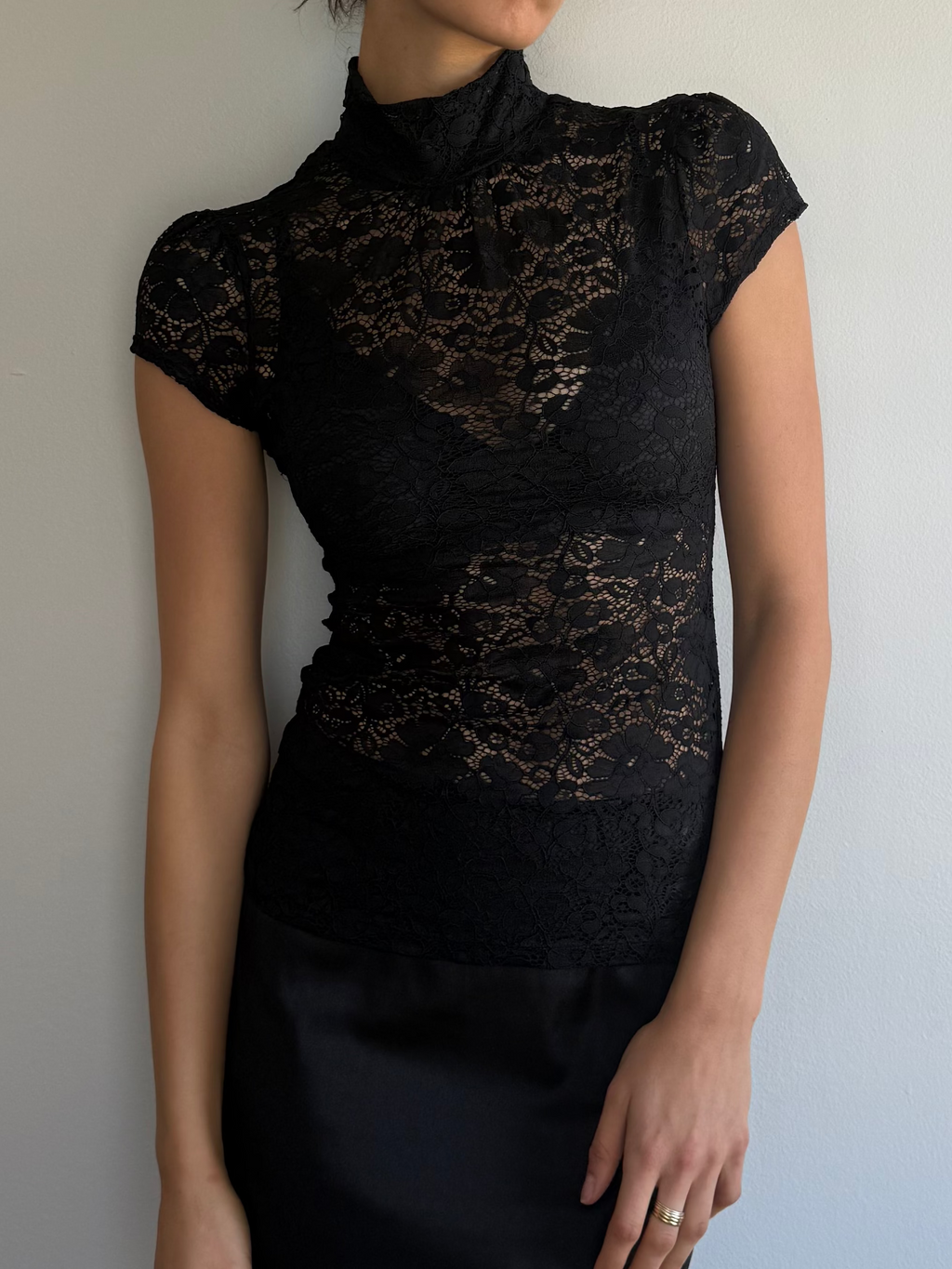 Woman wearing a black lace top and black skirt against a plain background