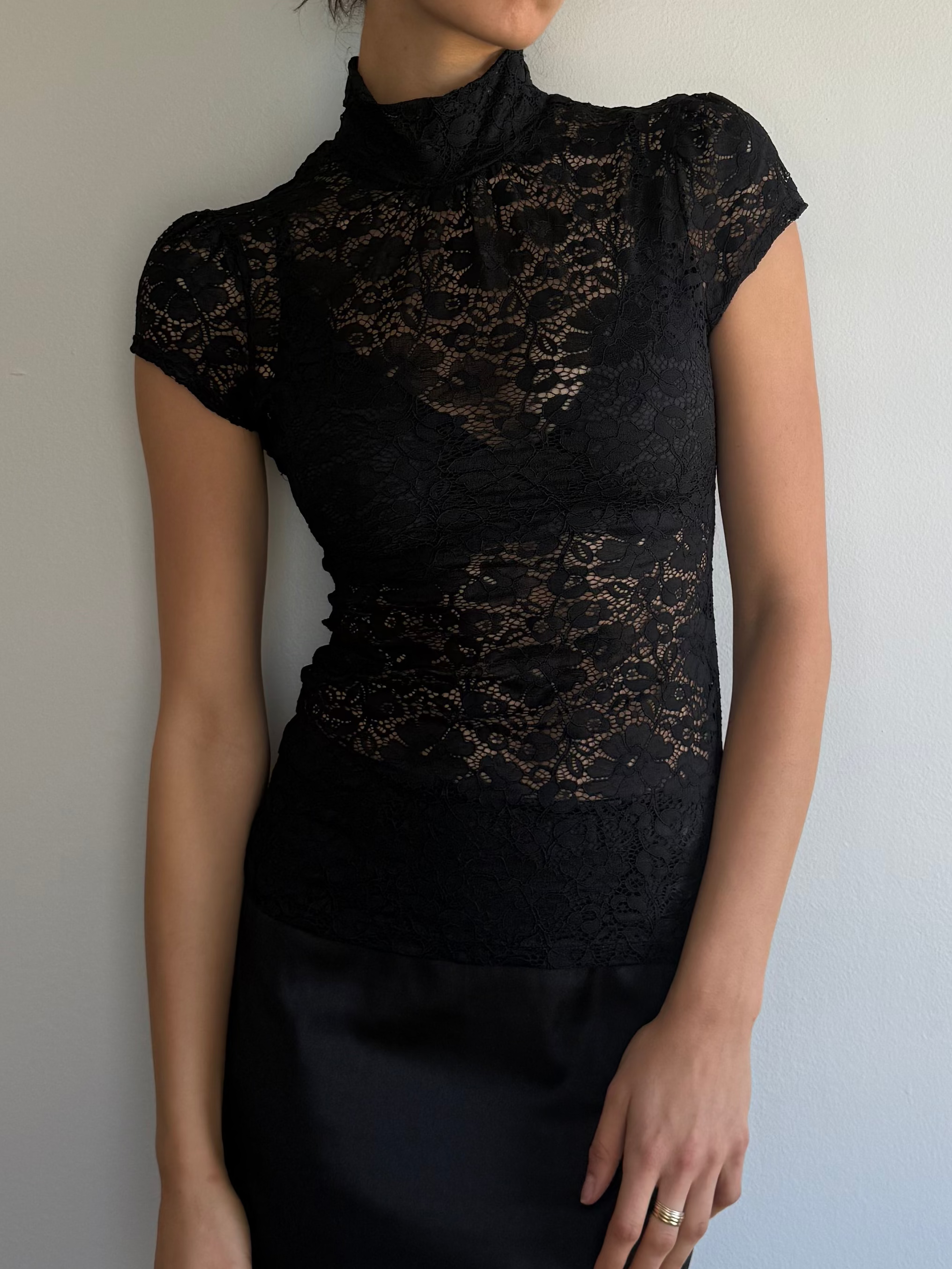 Woman wearing a black lace top and black skirt against a plain background