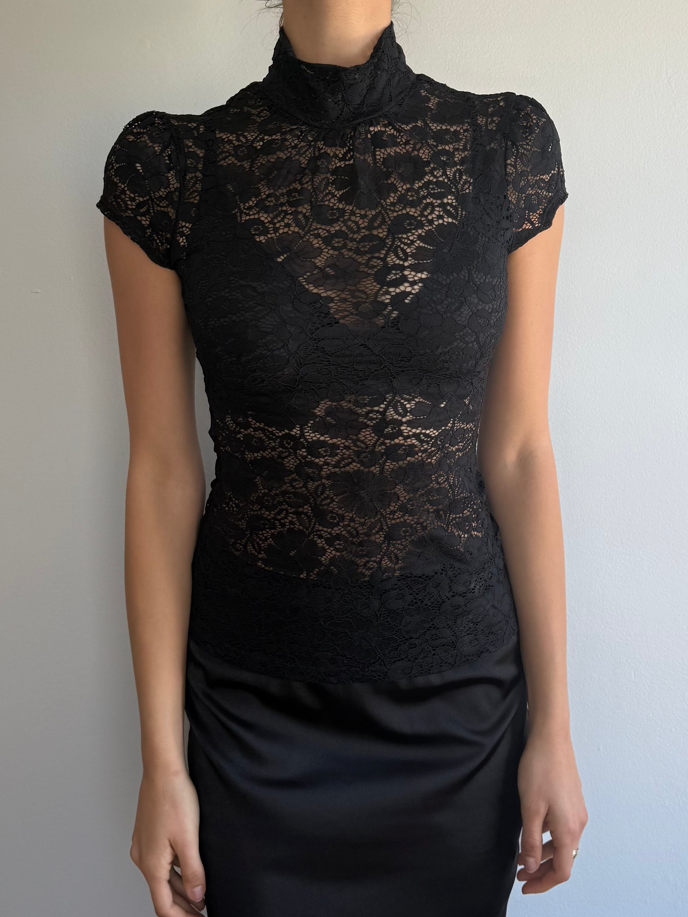Person wearing a black lace top and black skirt against a plain background