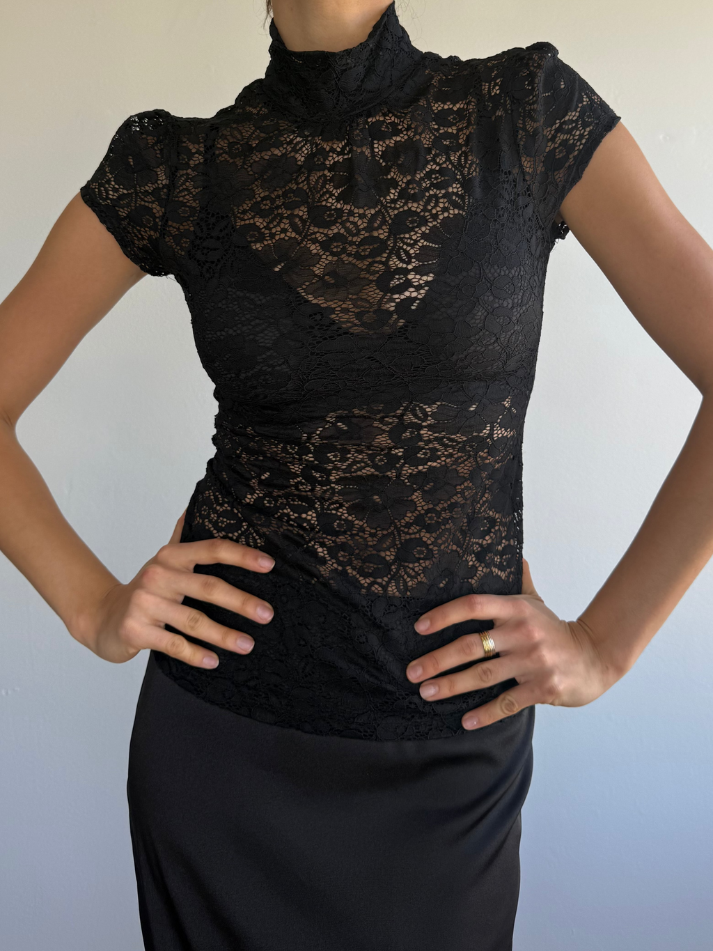 Woman wearing a black lace top against a plain background