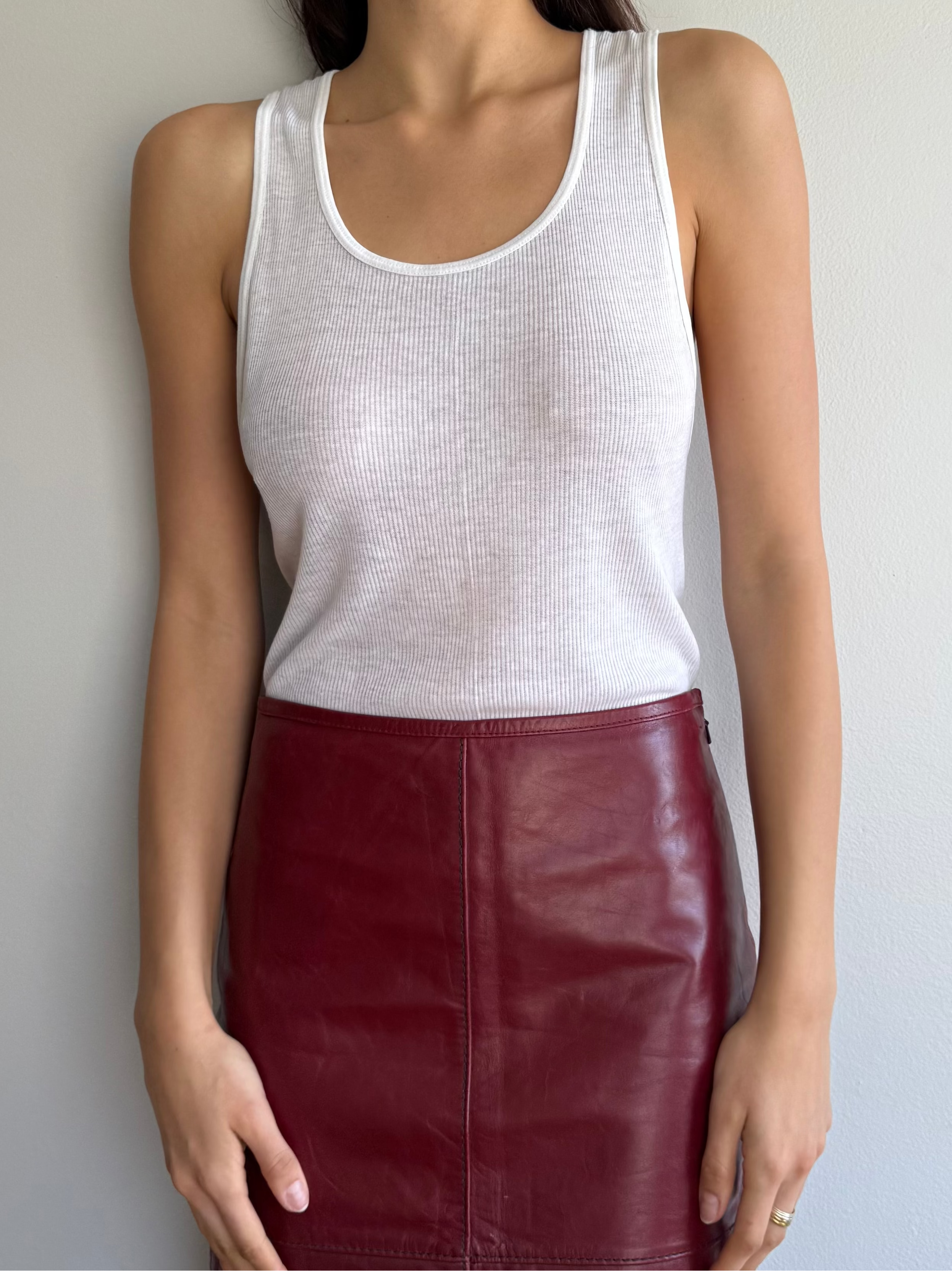 Person wearing a white tank top and red leather skirt against a neutral background