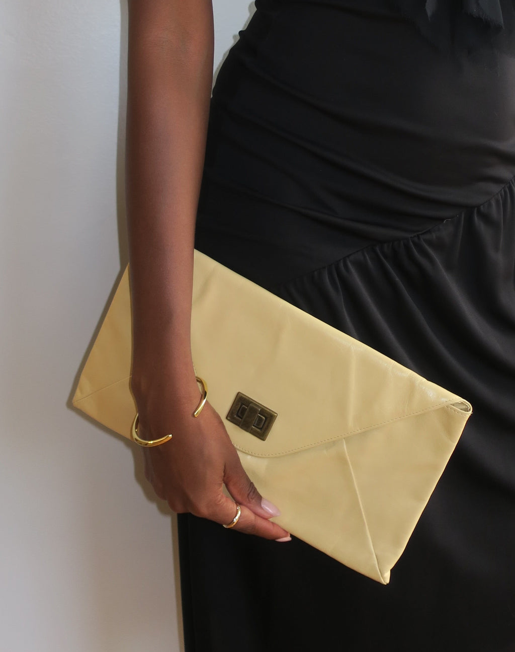 Woman in a black dress holding a gold clutch against a white background