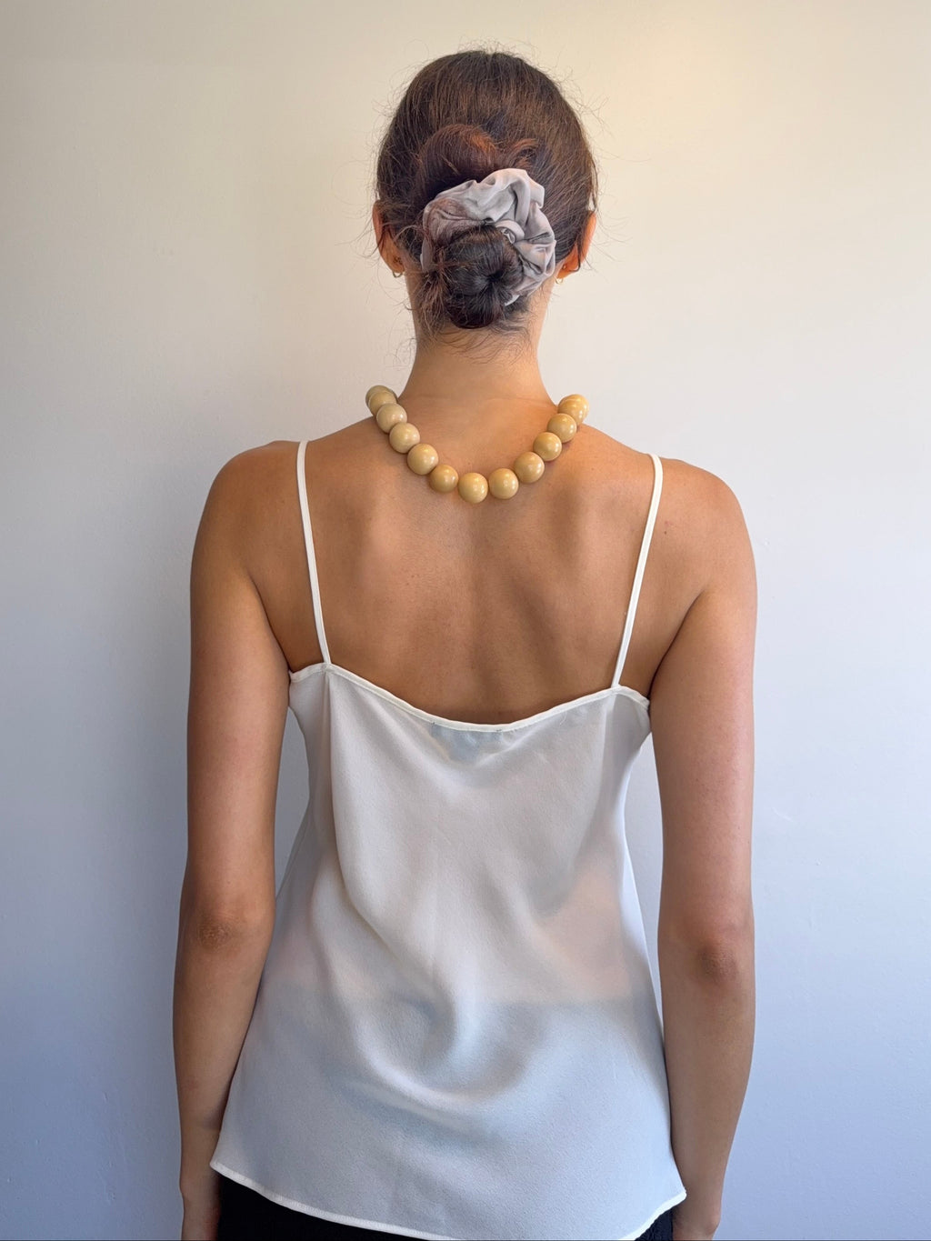 Person wearing a white spaghetti strap top with a plain background