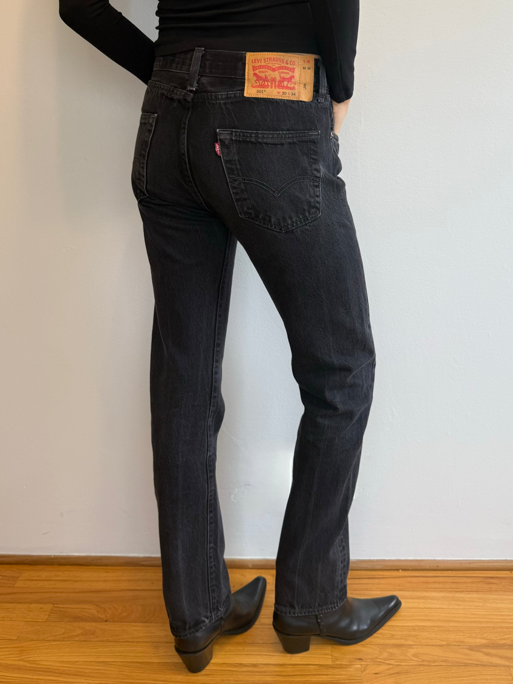 Person wearing black Levi's jeans standing against a plain wall.