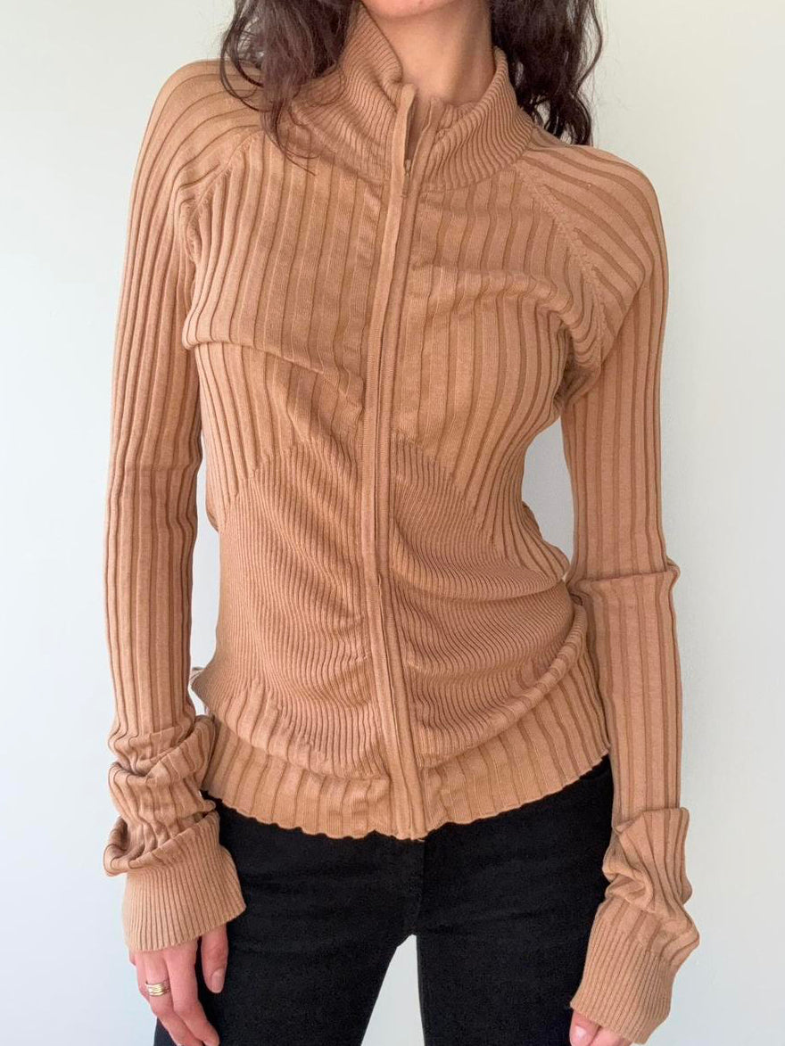 Person wearing a beige ribbed sweater against a white background